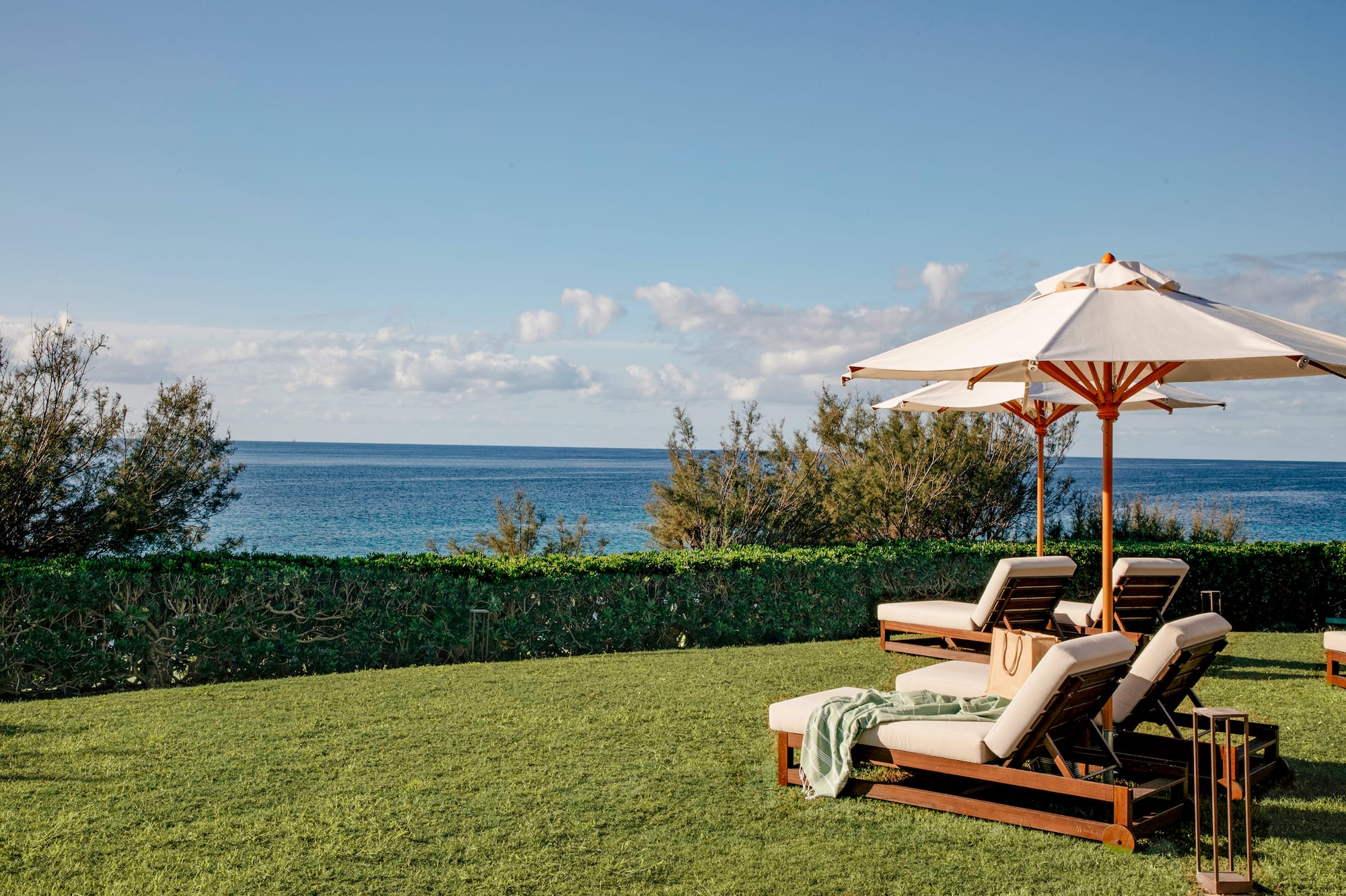 Tropical ocean view with green lawn, lounge chairs, and sun umbrellas.