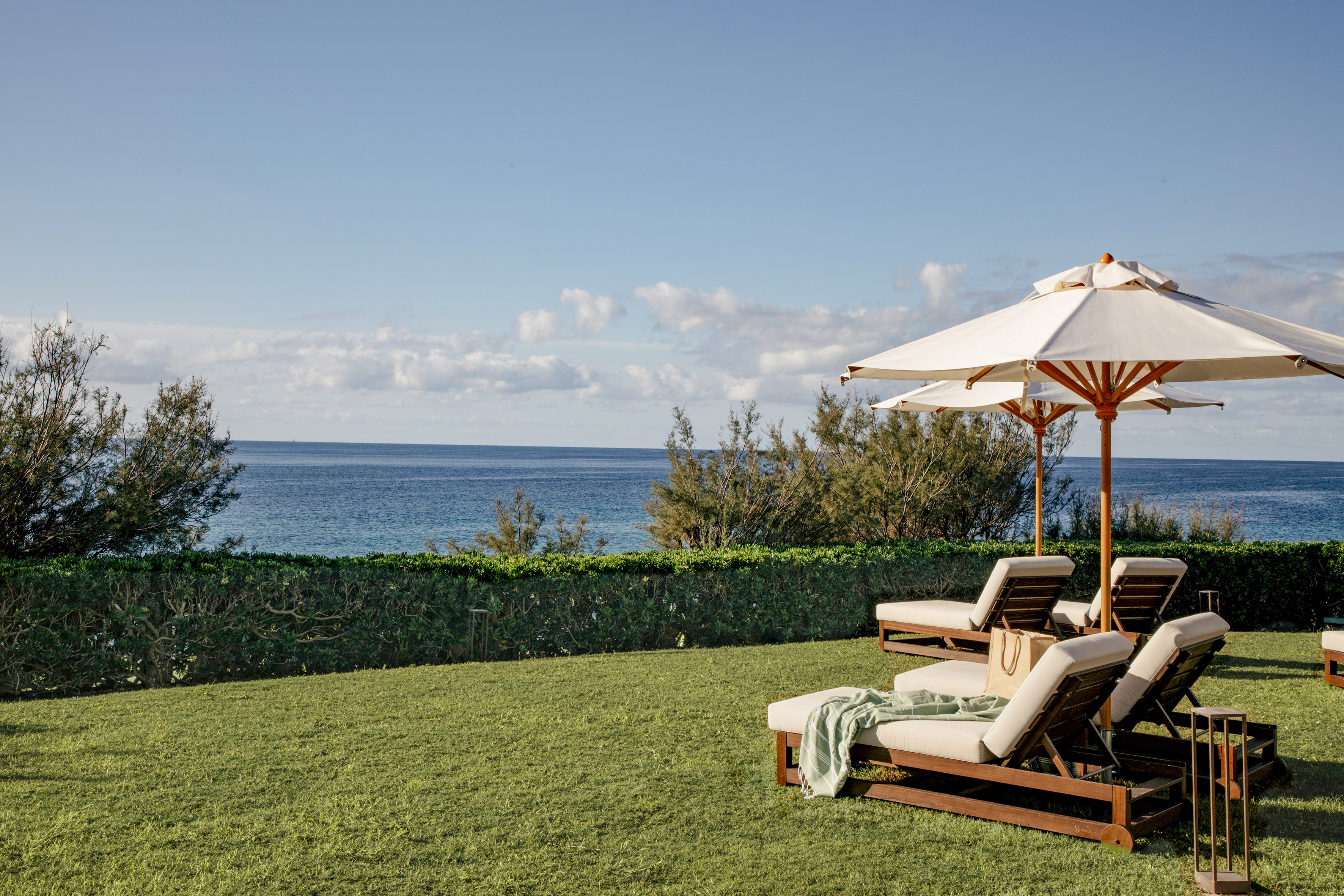 Tropical ocean view with green lawn, lounge chairs, and sun umbrellas.
