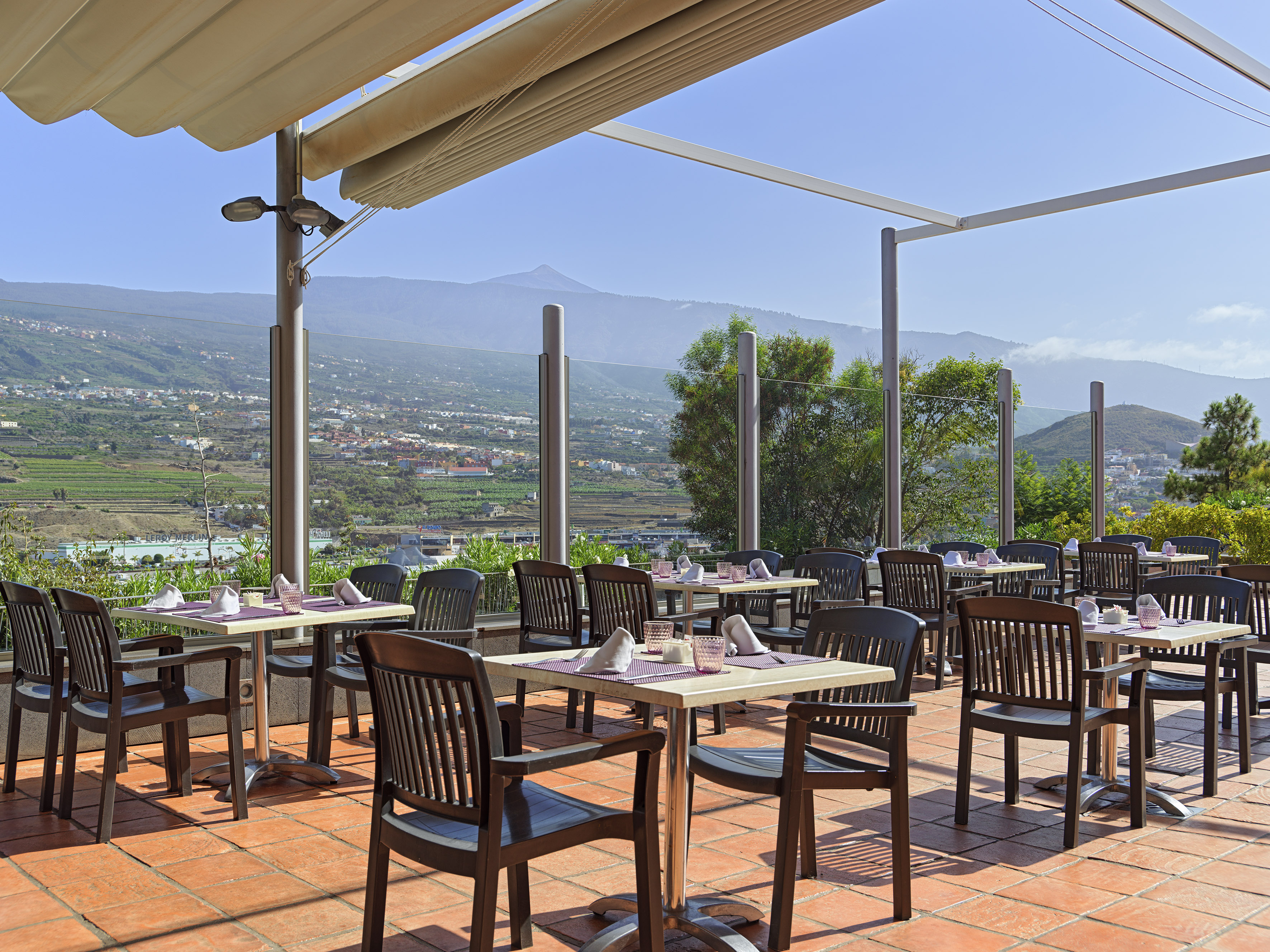 Outdoor dining terrace with scenic mountain view, set tables under an awning.