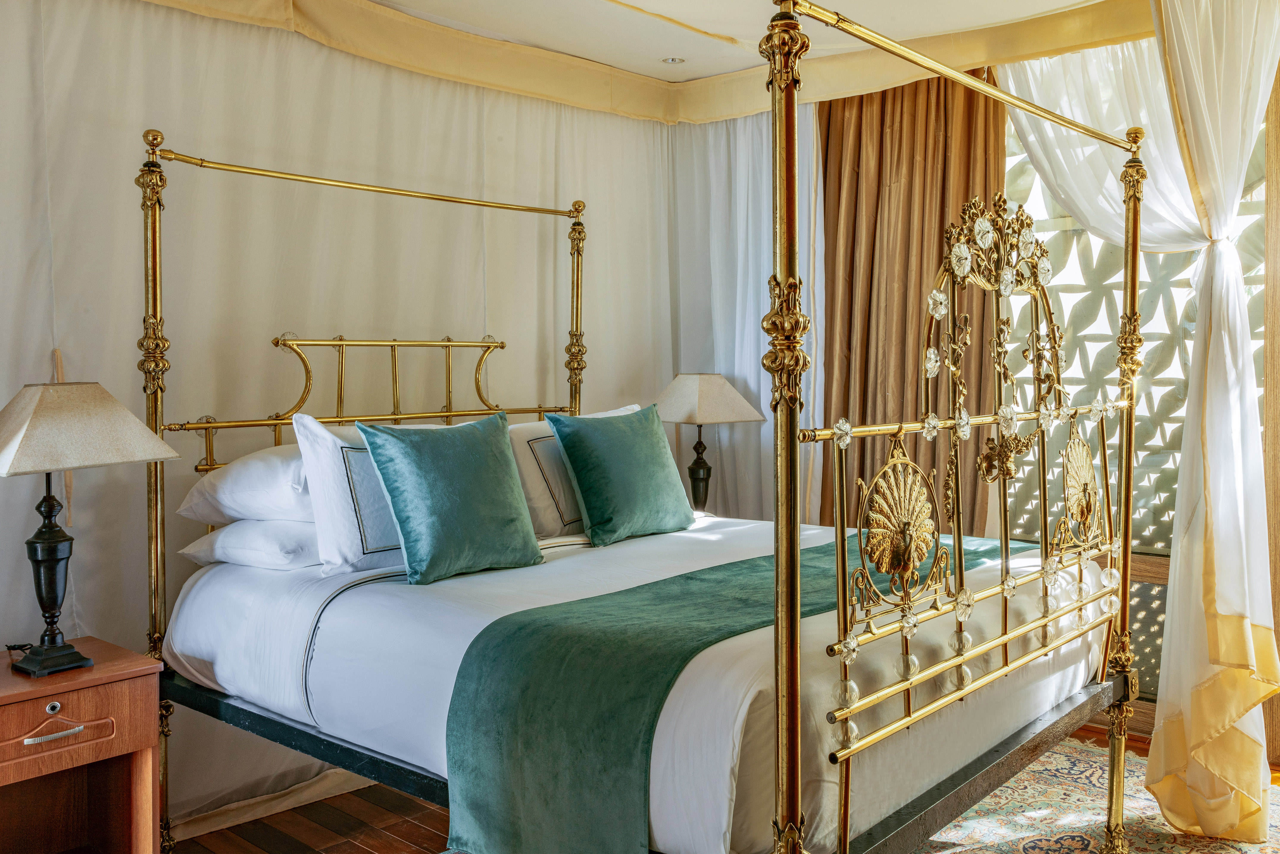Ornate vintage brass four-poster bed with teal bedding in a luxury bedroom.