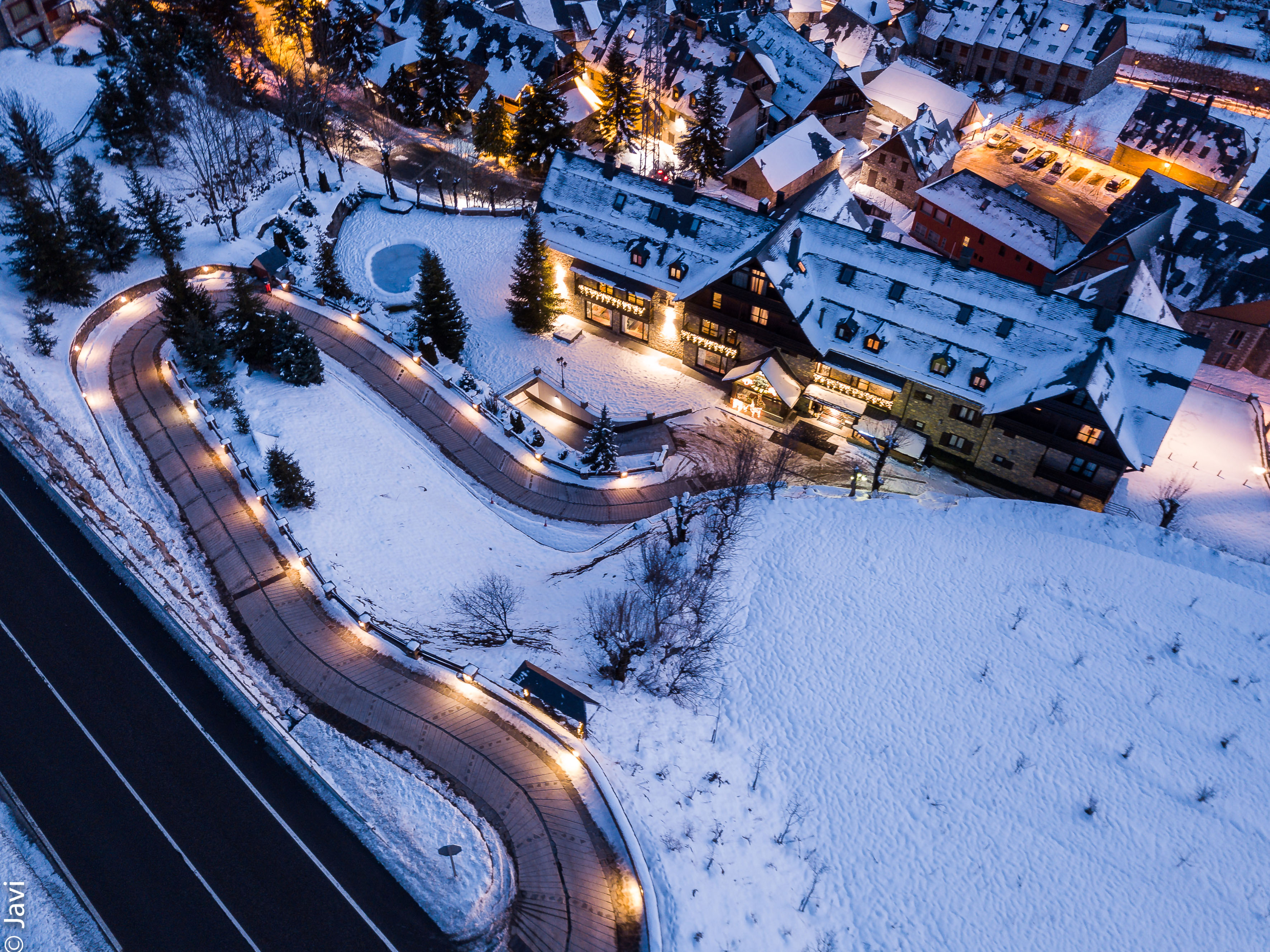 Aerial view: illuminated snowy mountain resort hotel and village at dusk.