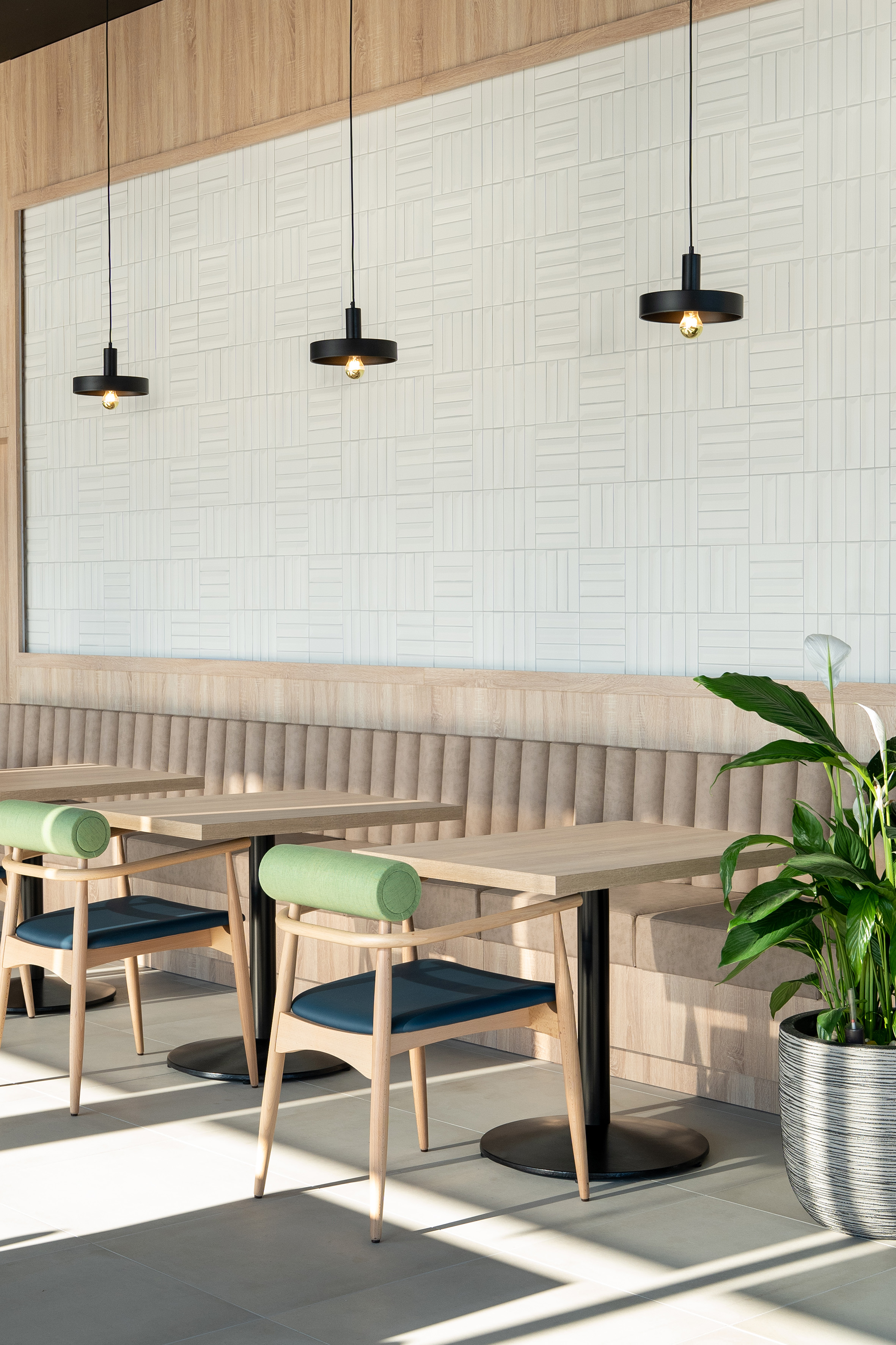 Modern cafe: geometric white tiles, wood, pendant lights, green chairs.