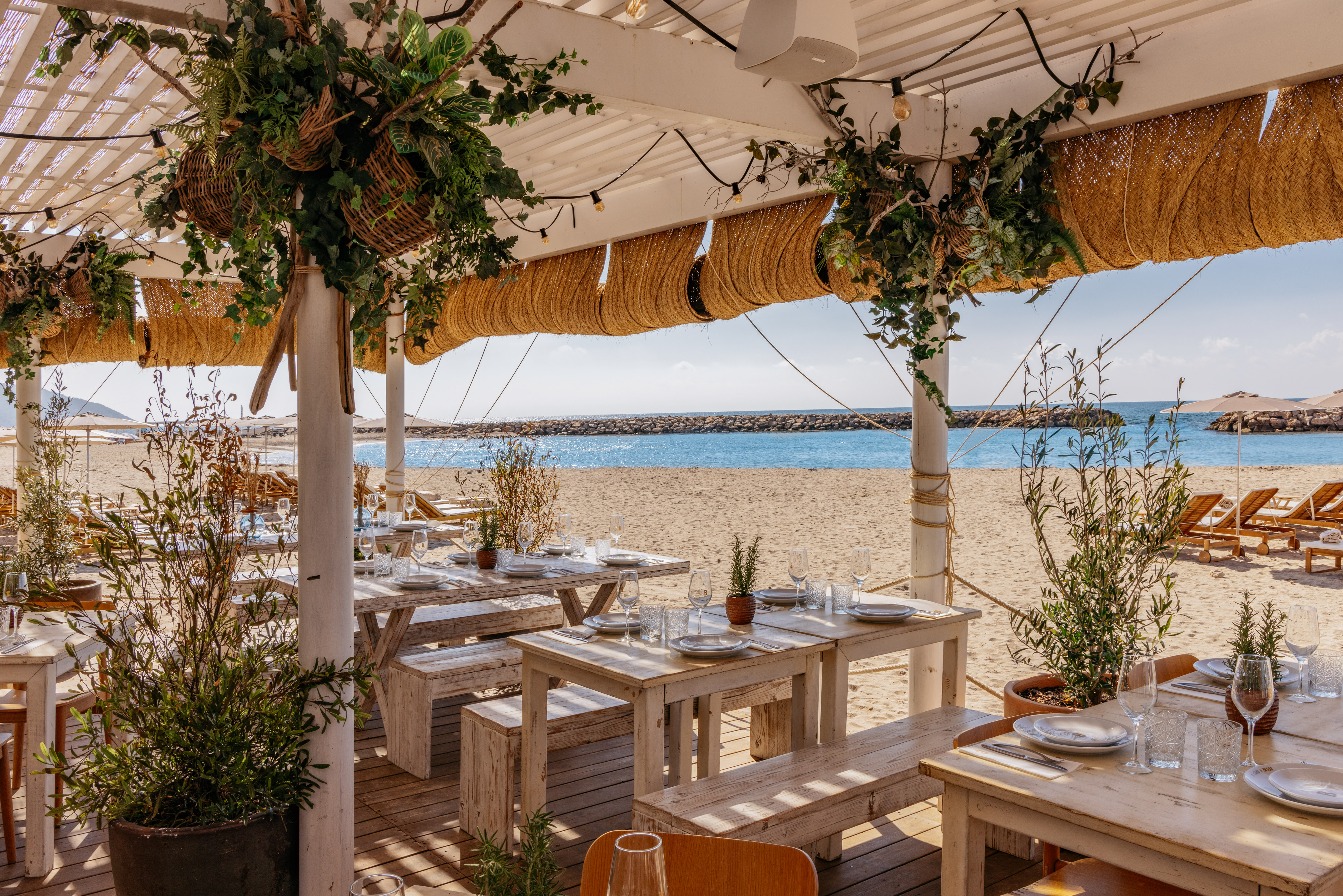 Beach restaurant with wooden tables, ocean view, and natural decor.