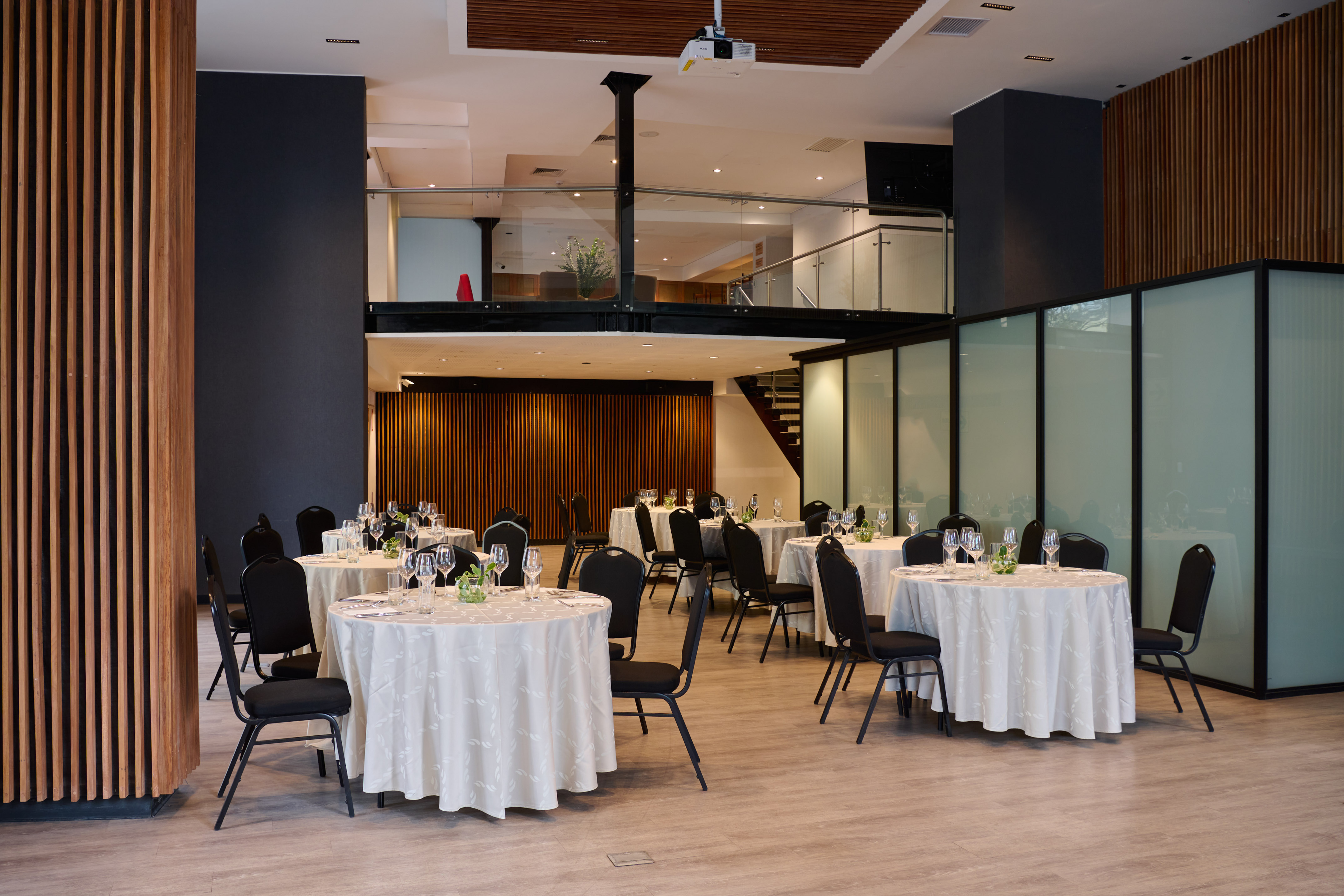 Hotel event room with set round tables, wood panels, and a mezzanine.