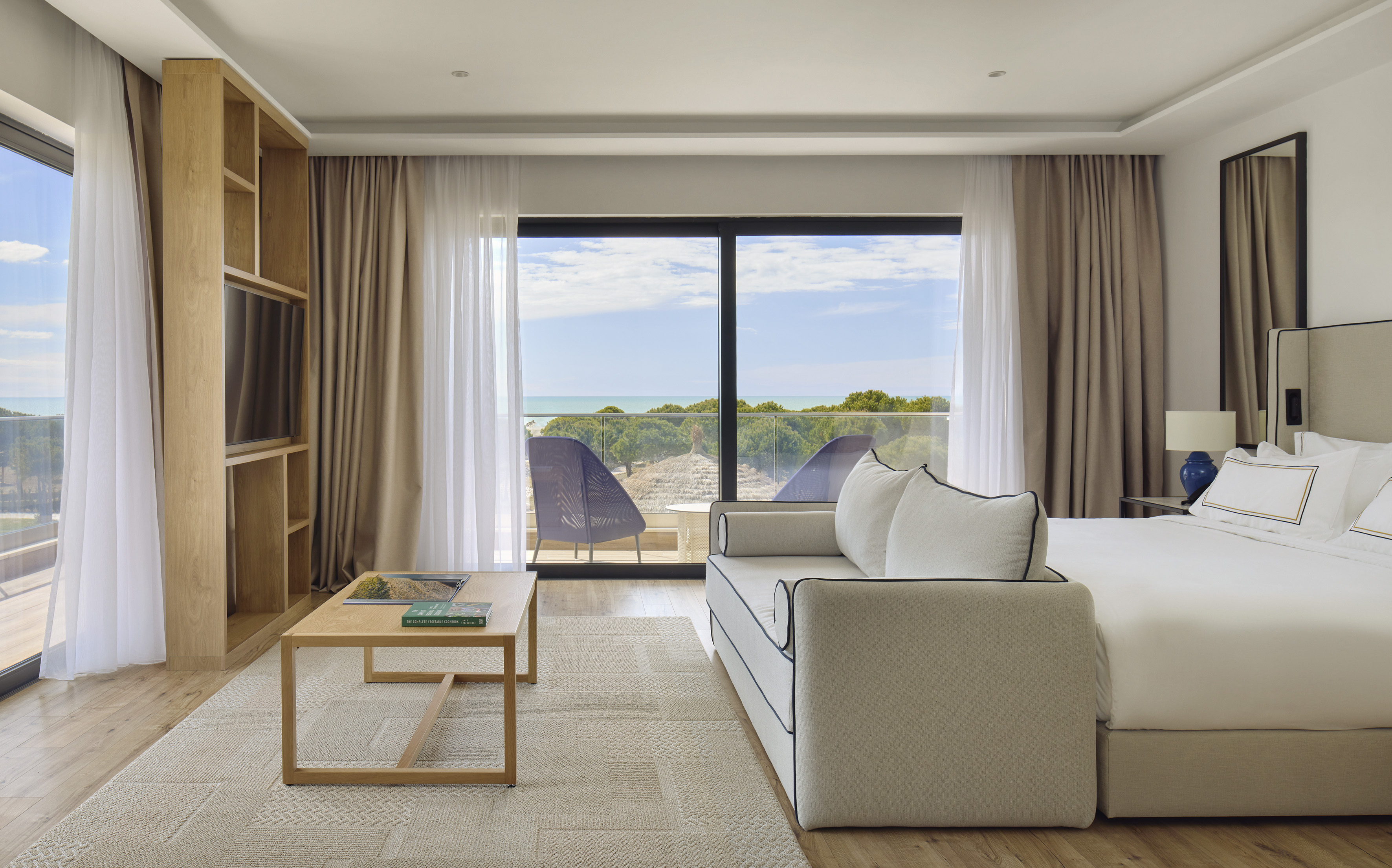 Luxury hotel suite with ocean view balcony, bed, and sofa.