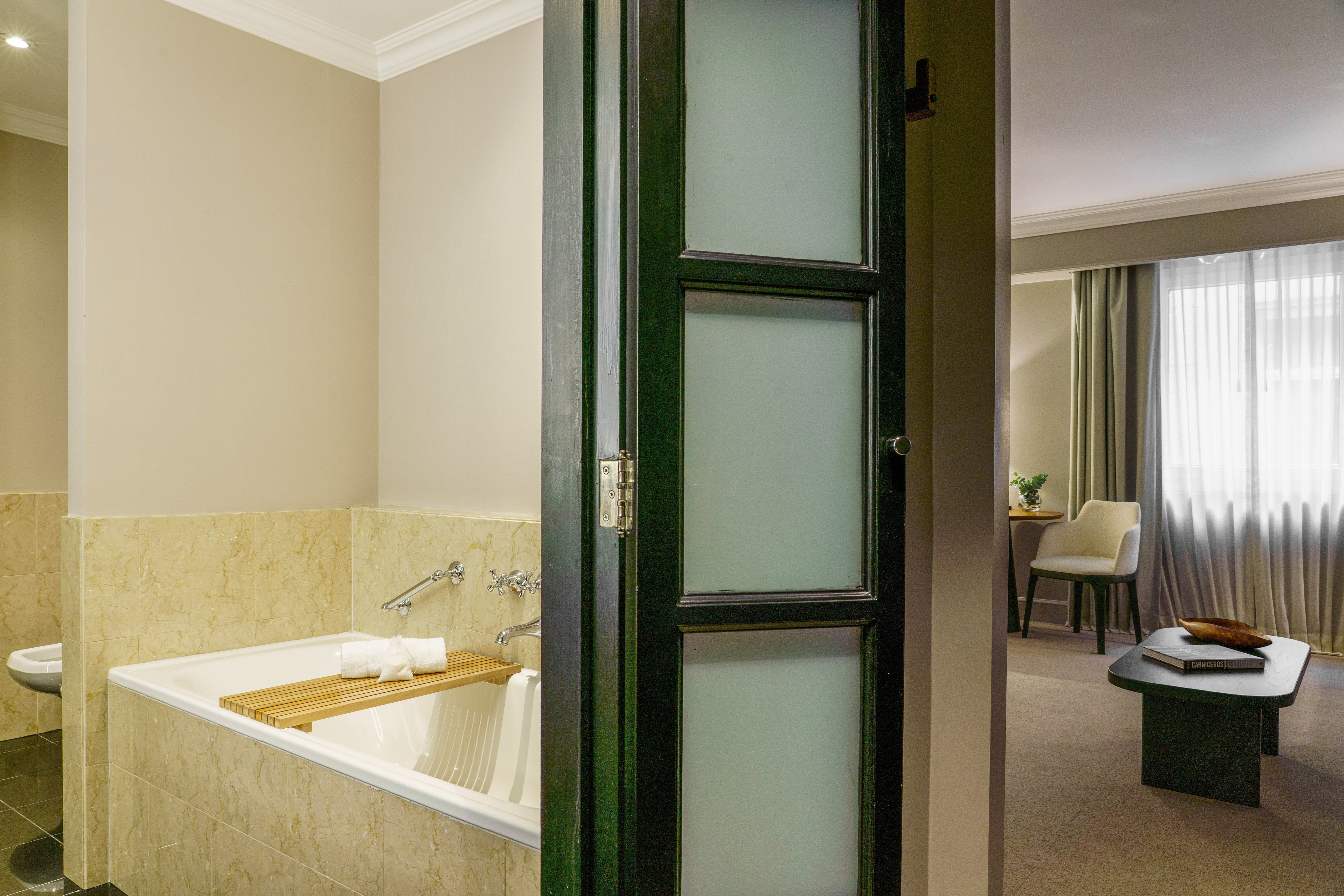 Hotel suite bathroom with marble tub, dark door to bedroom.