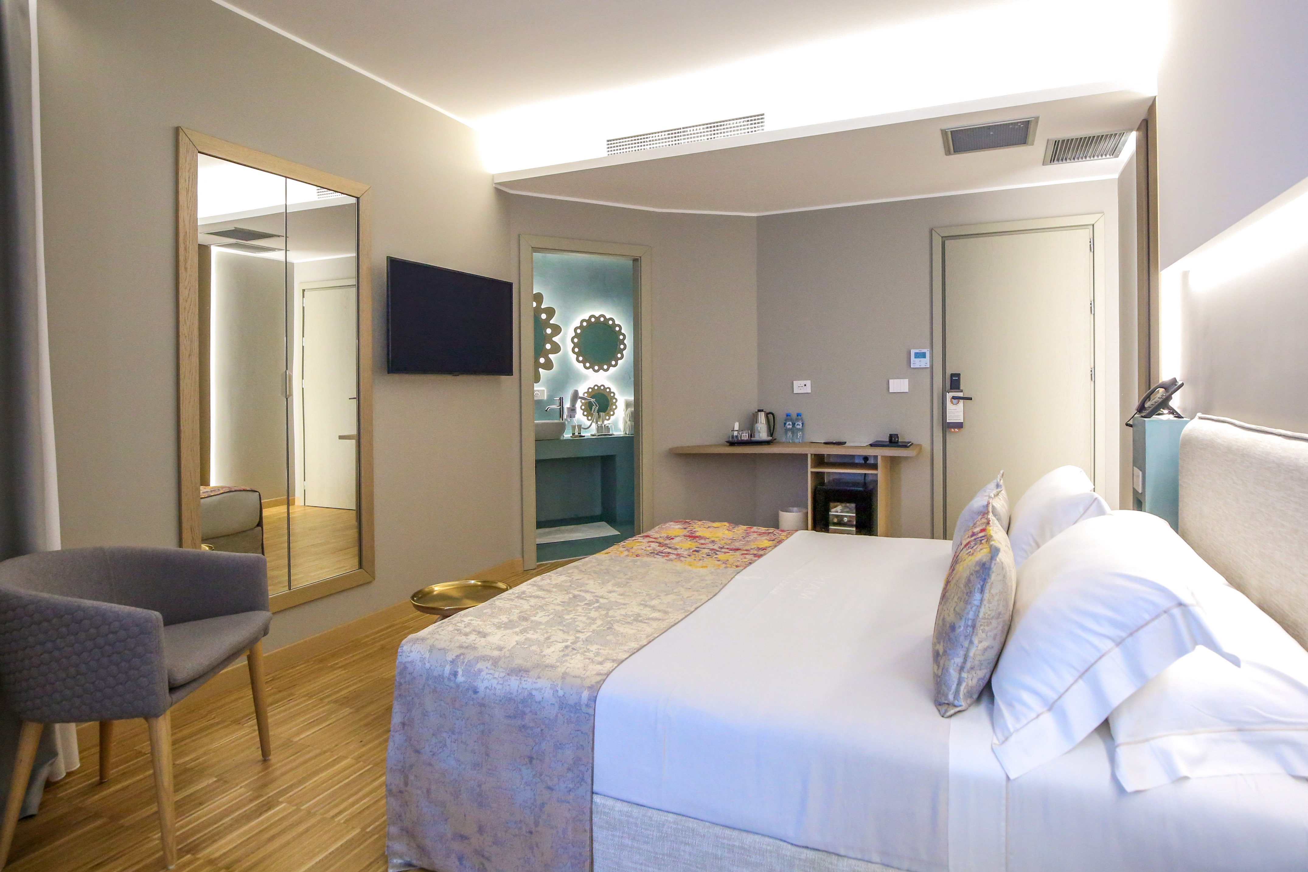 Modern hotel room with king bed, TV, armchair, and en-suite bathroom.