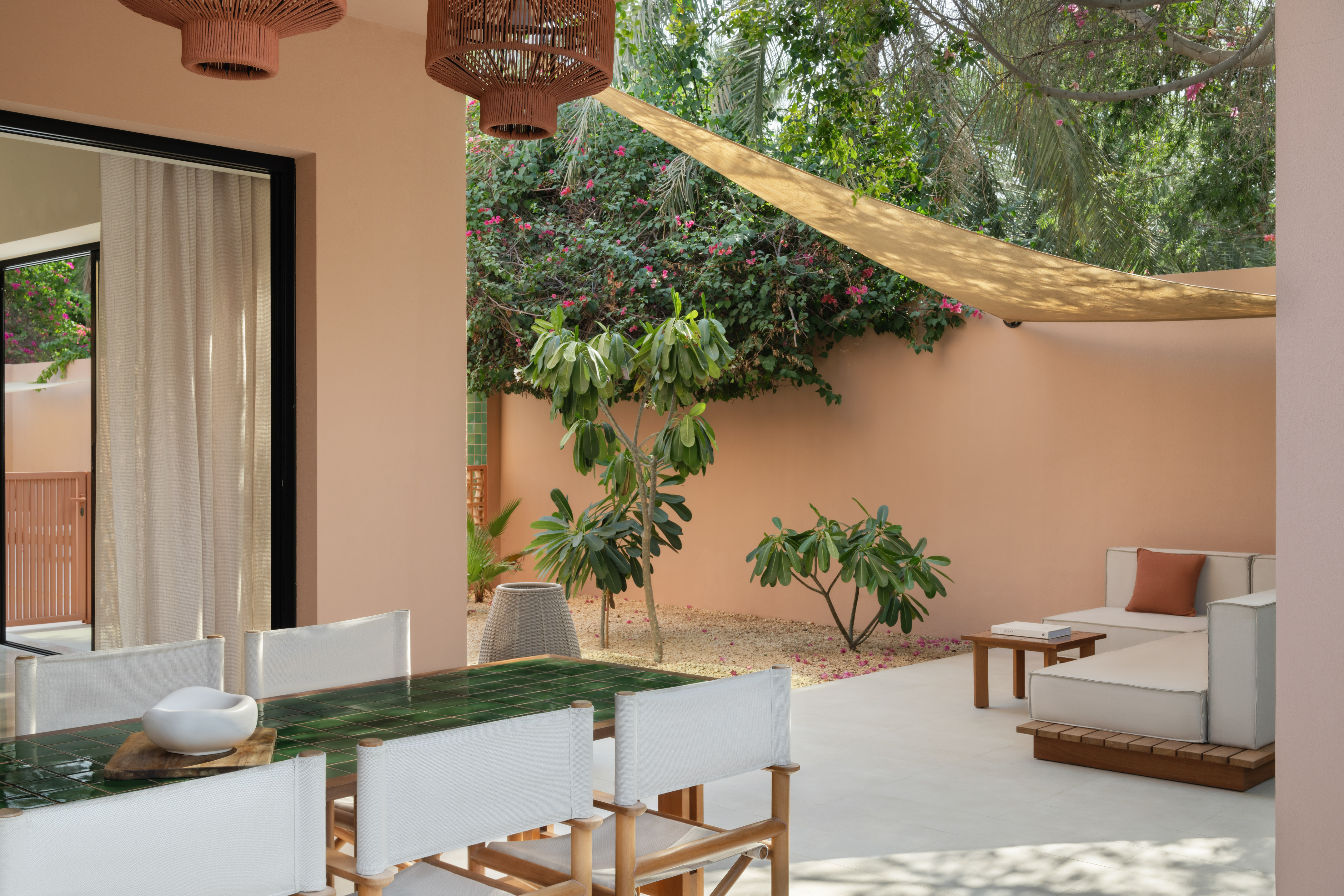 Modern outdoor patio with green tiled dining table, lounge, and lush garden.