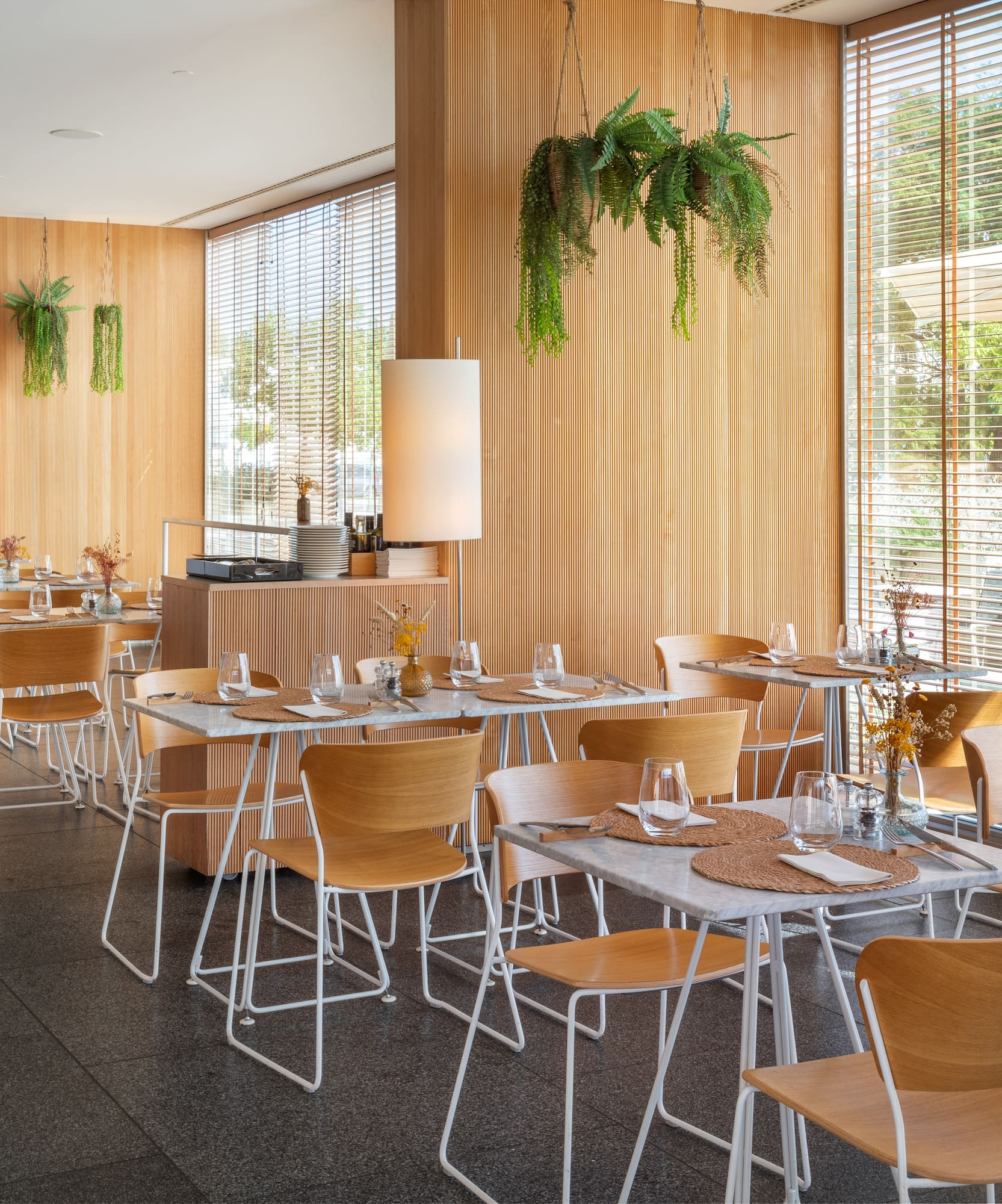 Restaurante moderno, interior luminoso. Paneles de madera, mesas de mármol y plantas.