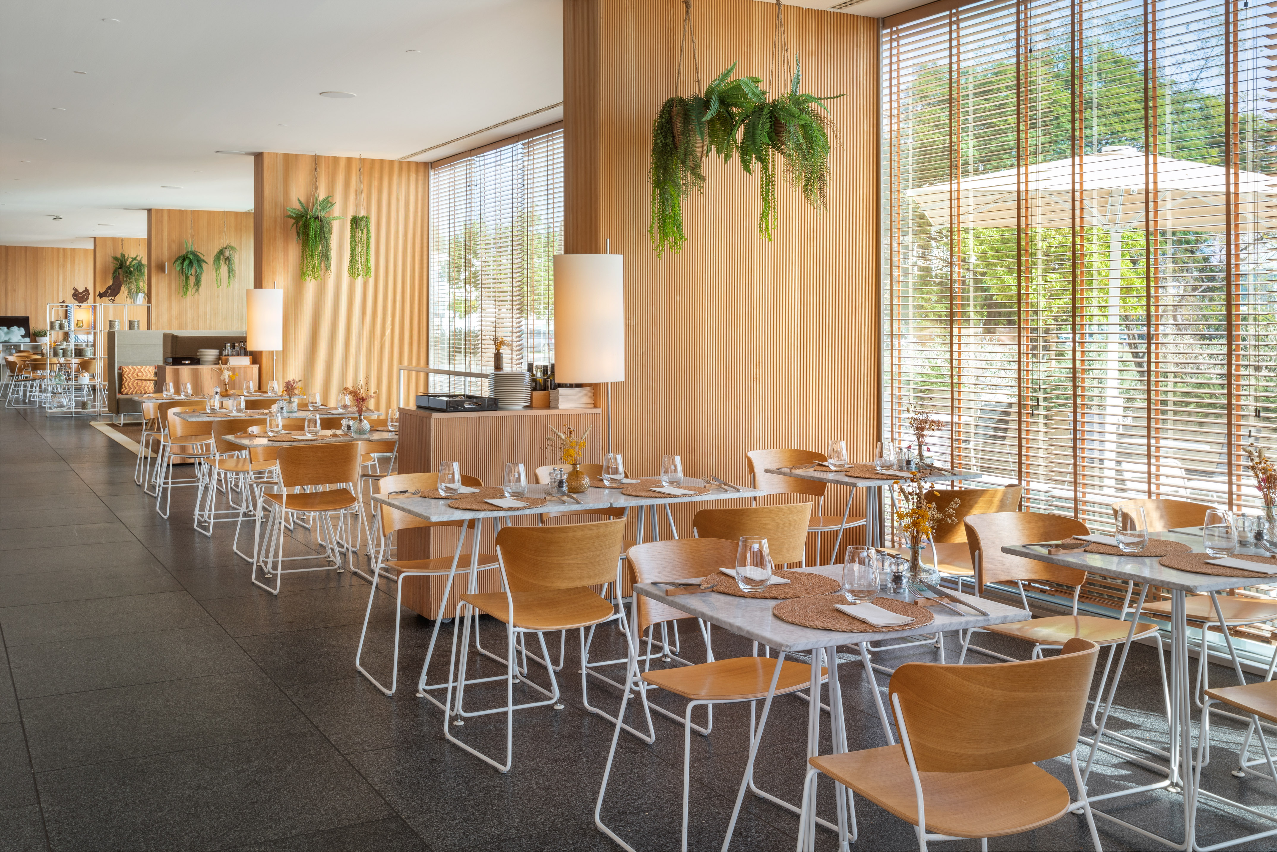 Restaurante moderno, interior luminoso. Paneles de madera, mesas de mármol y plantas.