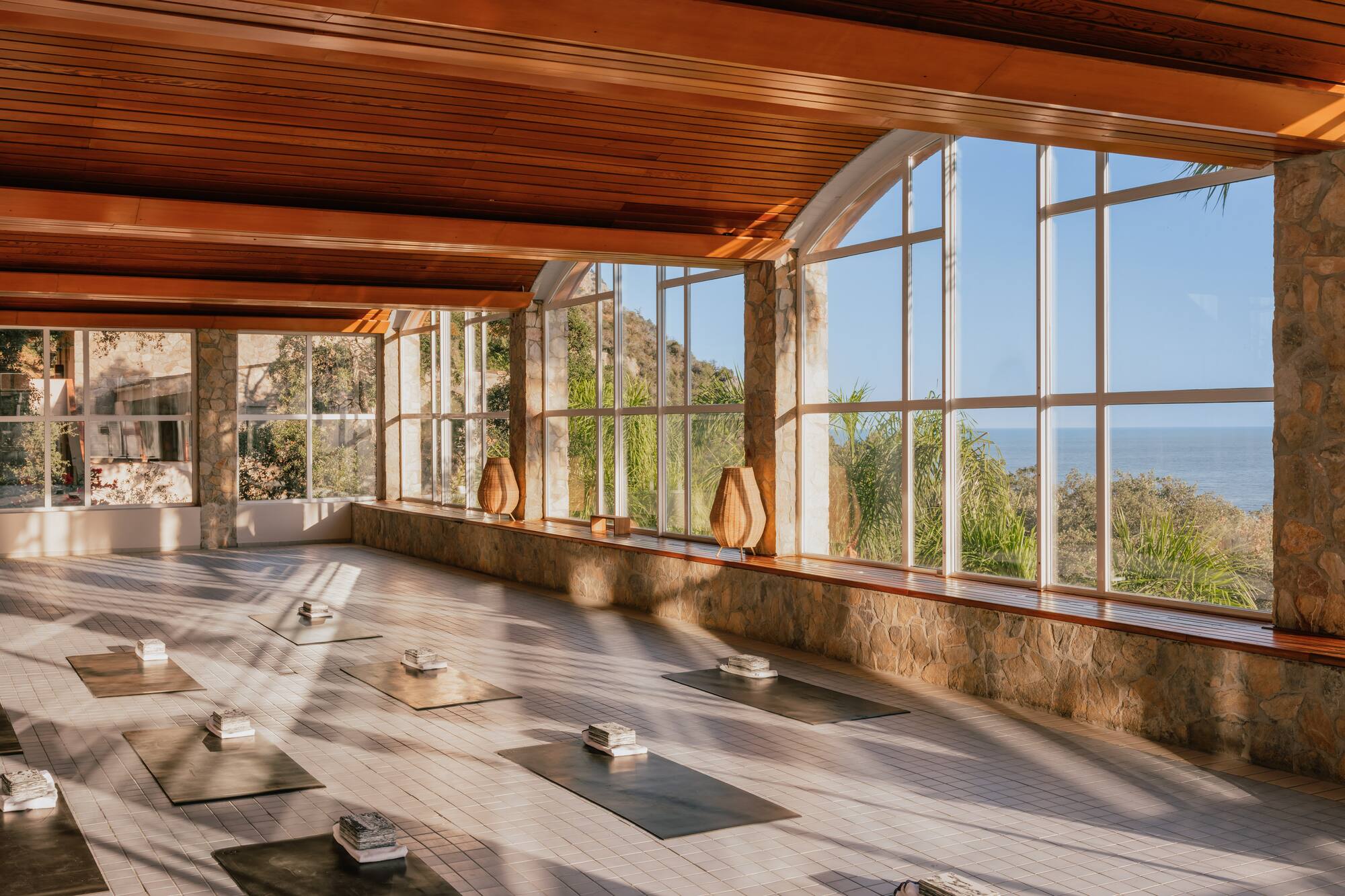 Ocean view yoga studio with natural light, wooden ceiling, and yoga mats.