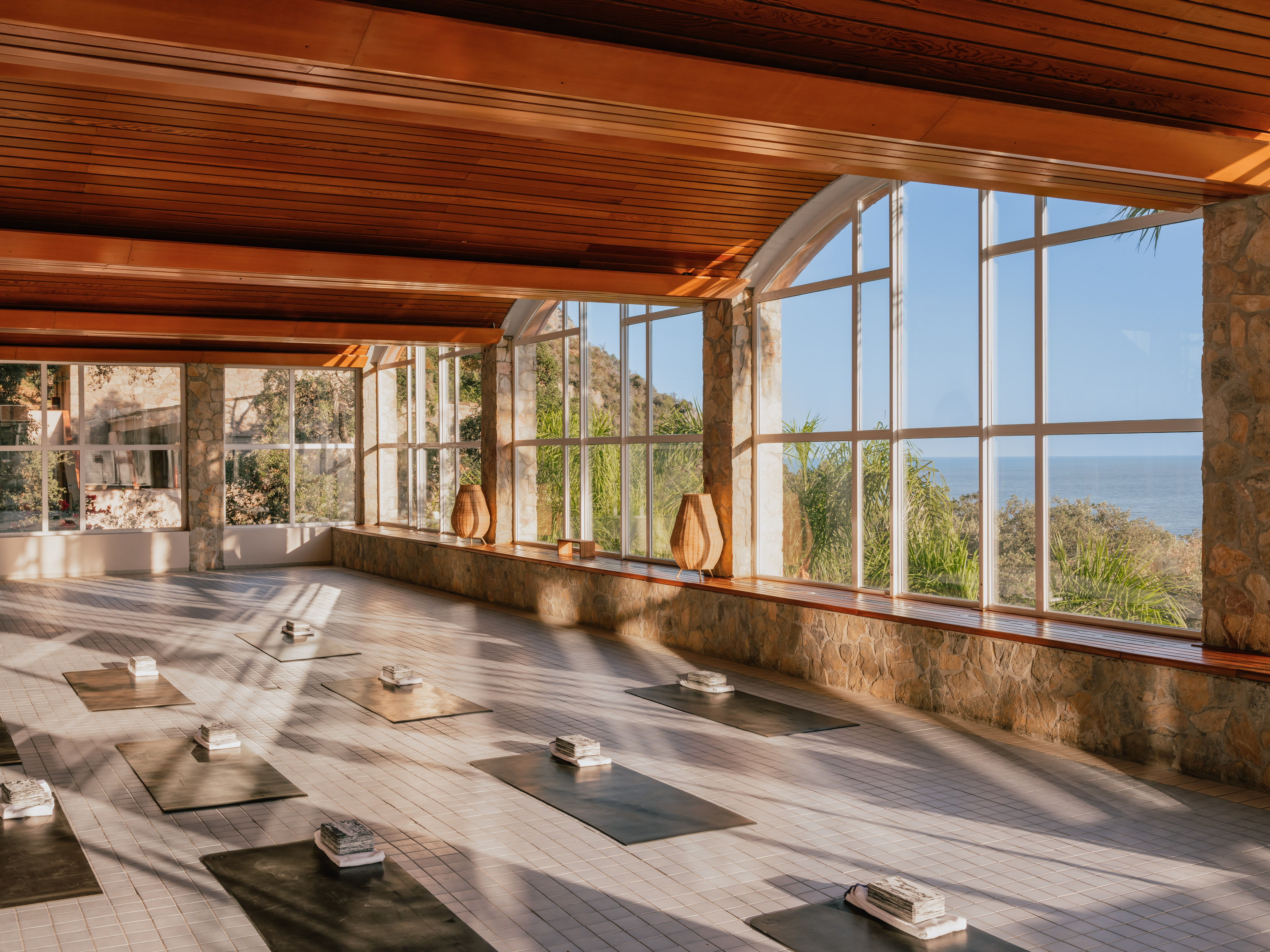 Ocean view yoga studio with natural light, wooden ceiling, and yoga mats.