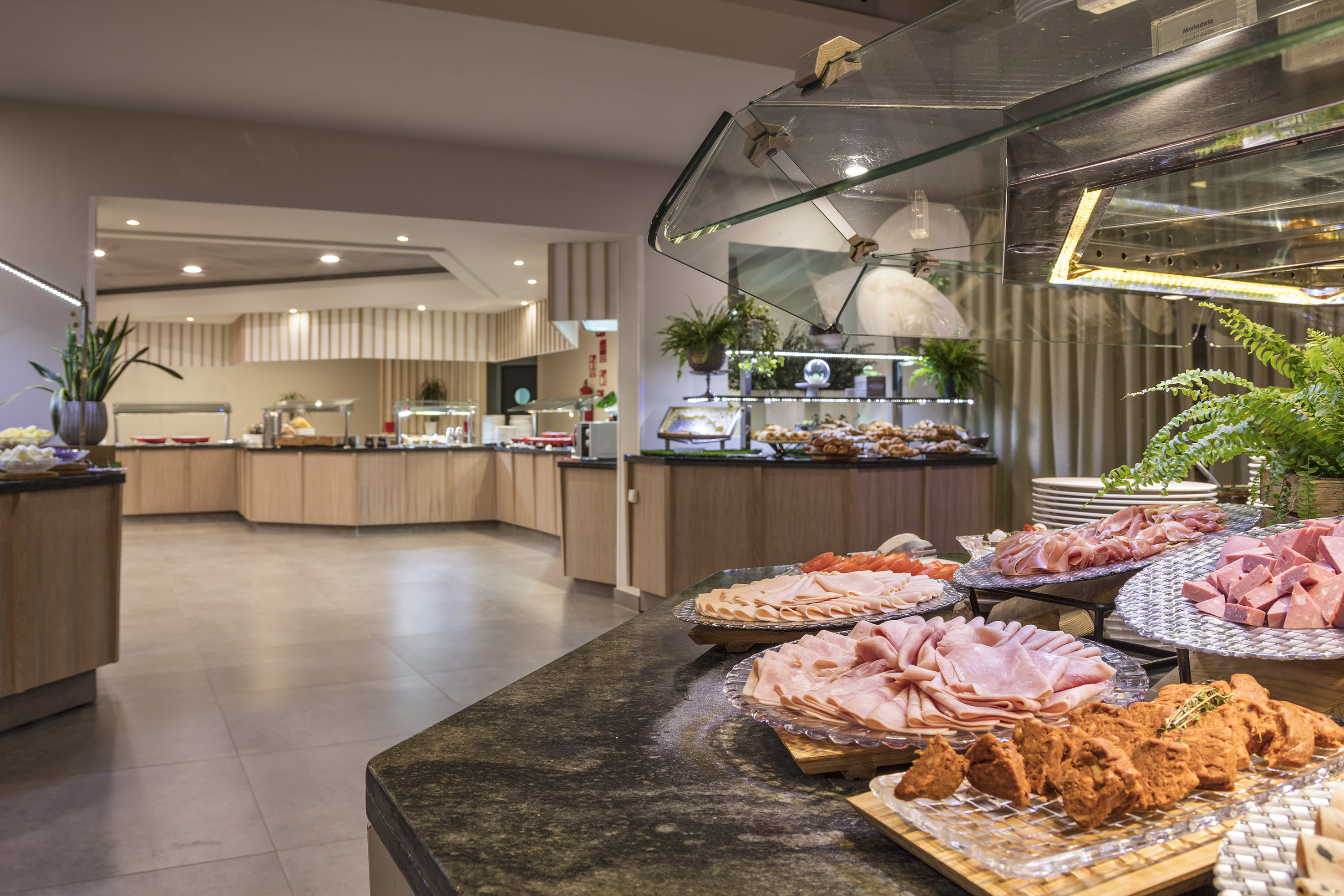 Hotel buffet with sliced ham, mortadella, other cold cuts, and pastries.