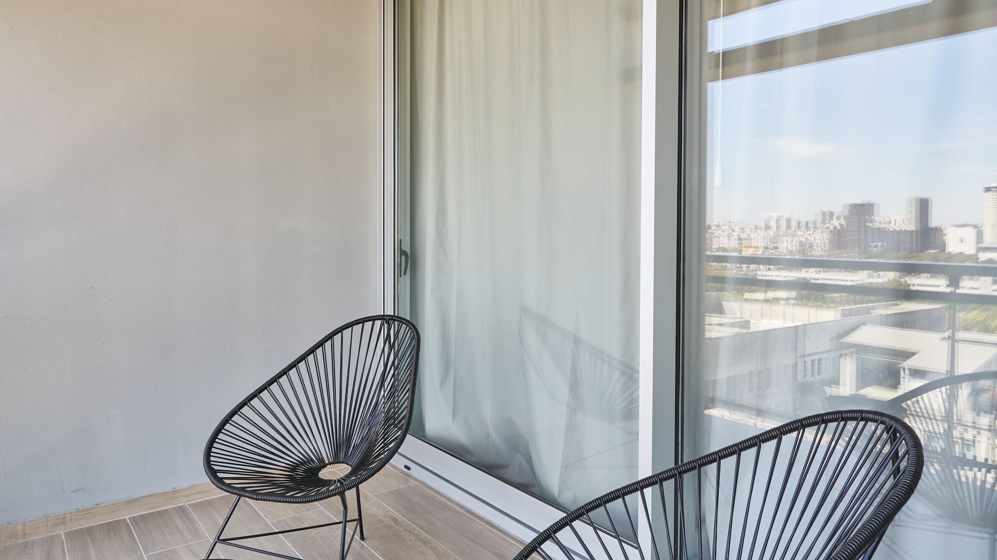 Modern apartment balcony featuring black Acapulco chairs and a city skyline view.