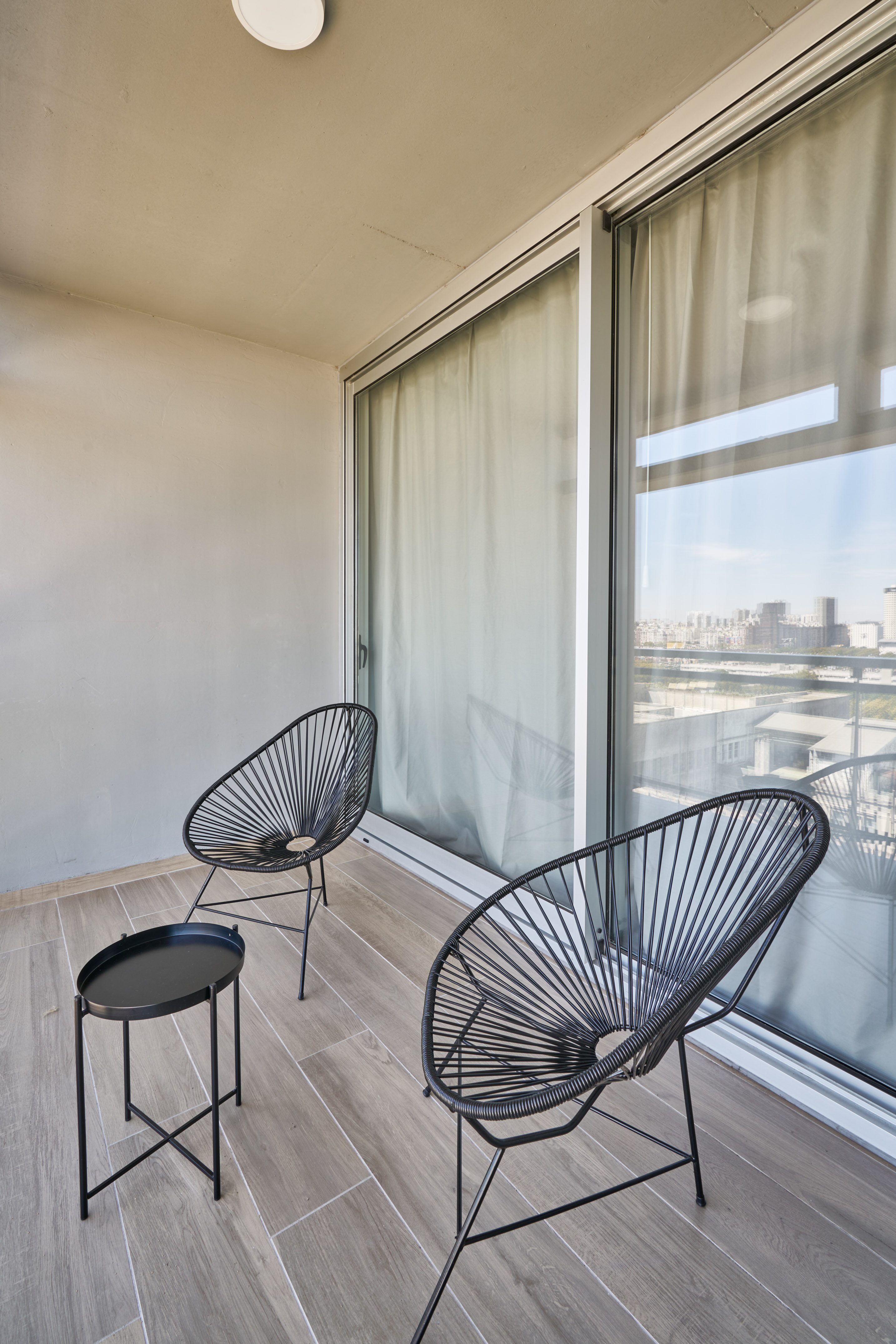 Modern apartment balcony featuring black Acapulco chairs and a city skyline view.