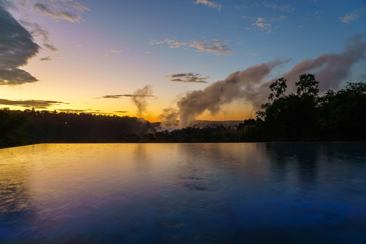 a body of water with trees and clouds in the sky