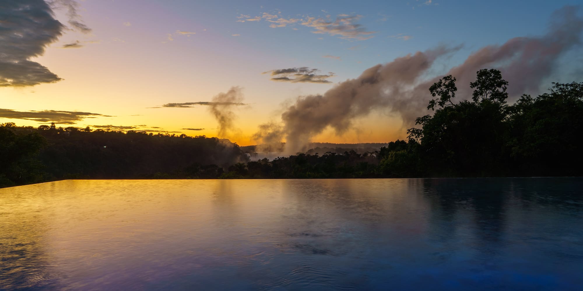 a body of water with trees and clouds in the sky