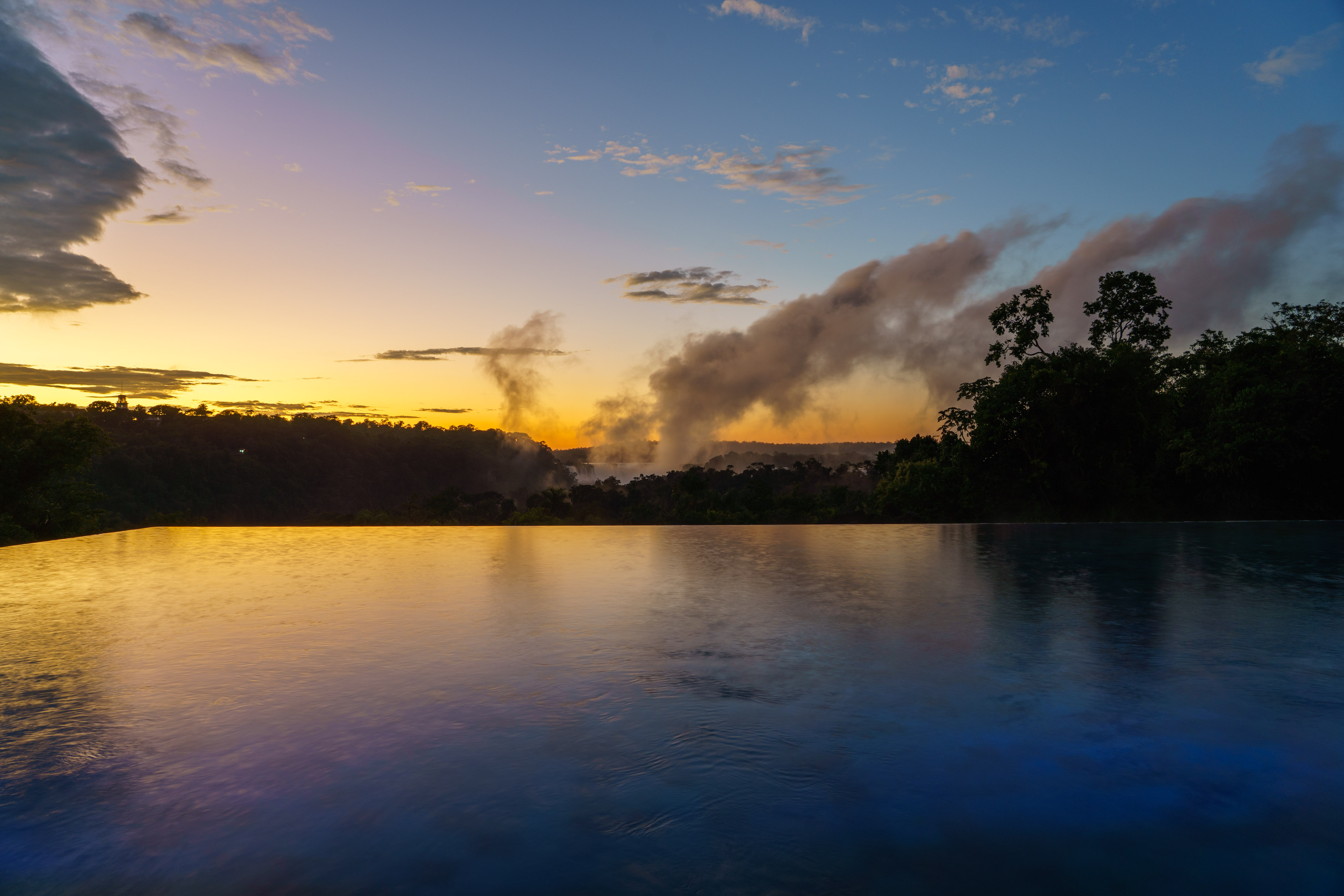 Sunset over infinity pool, rainforest, and misty Iguazu Falls.