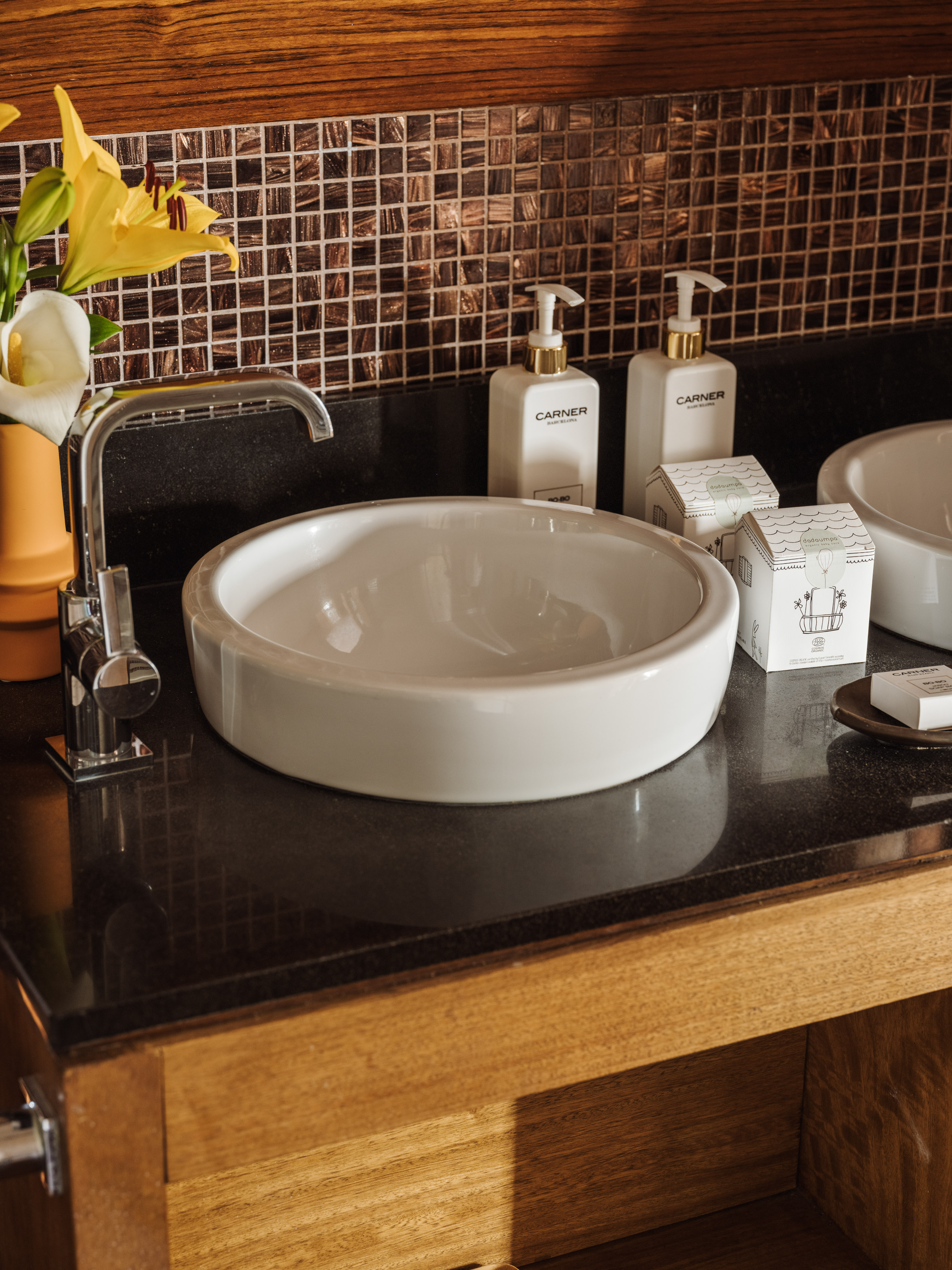 Modern bathroom vanity with white sink, chrome faucet, toiletries, mosaic backsplash.