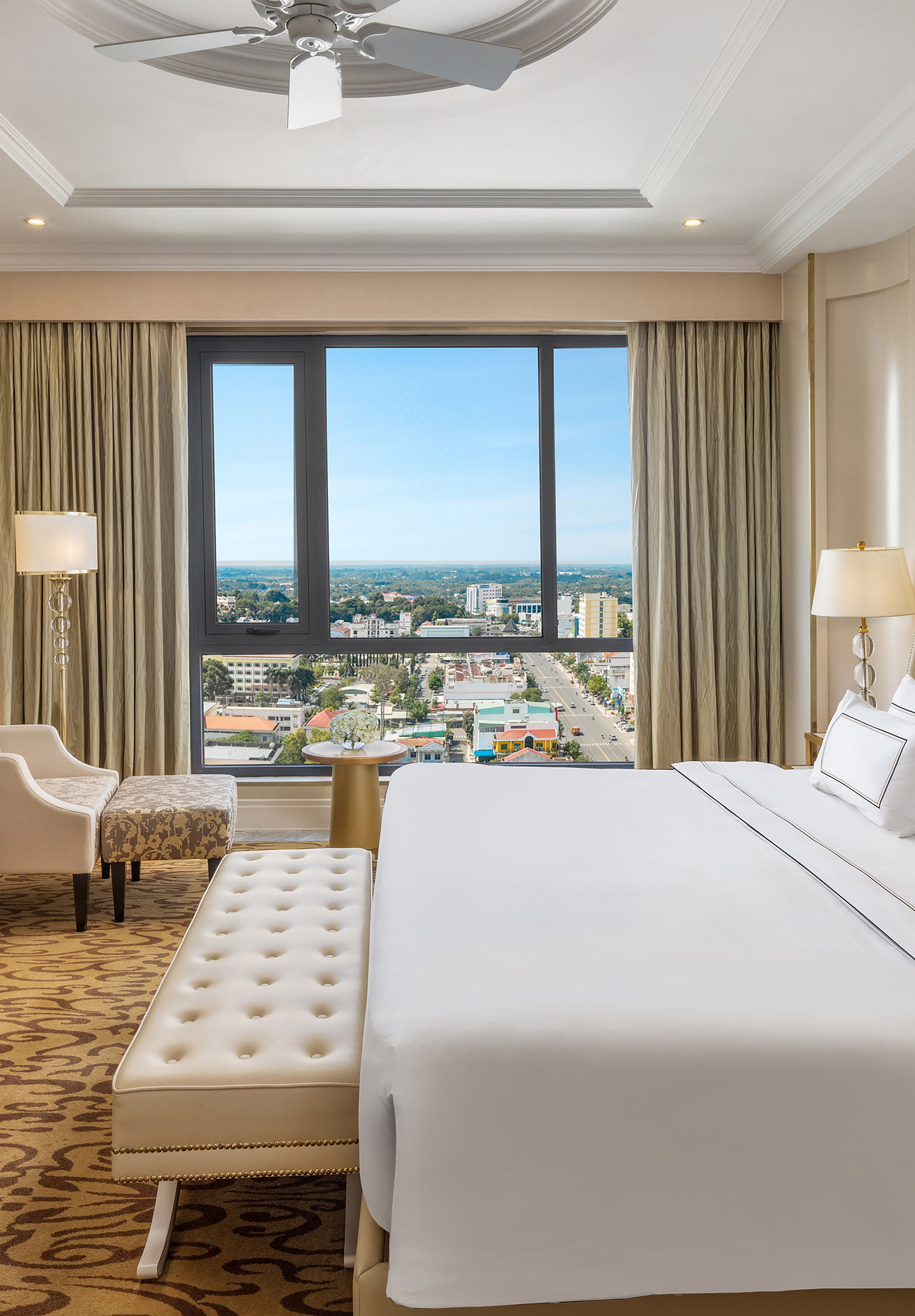 Luxury hotel bedroom with city view, large bed, and elegant decor.
