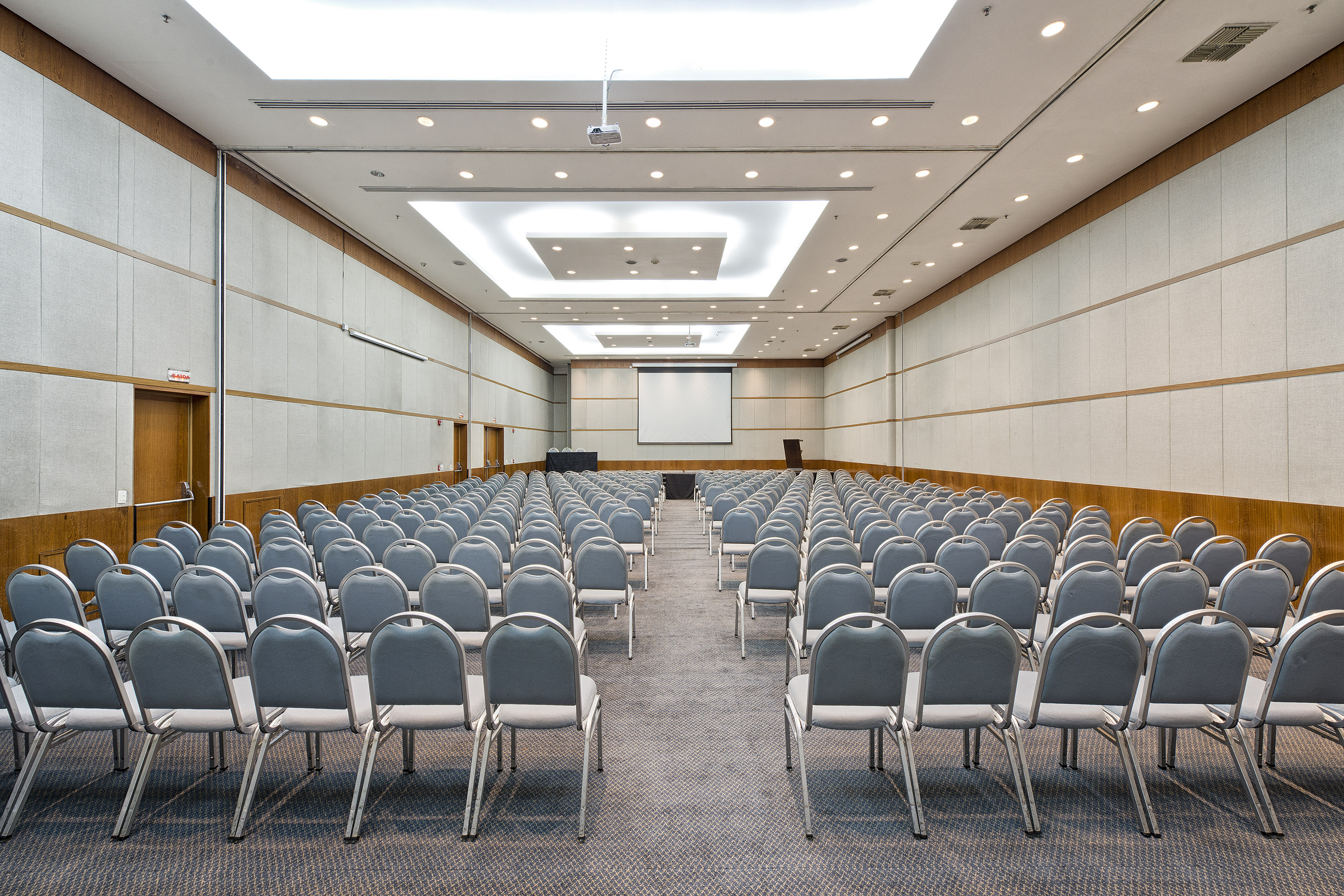 Empty hotel ballroom with rows of chairs, projector, and large screen.