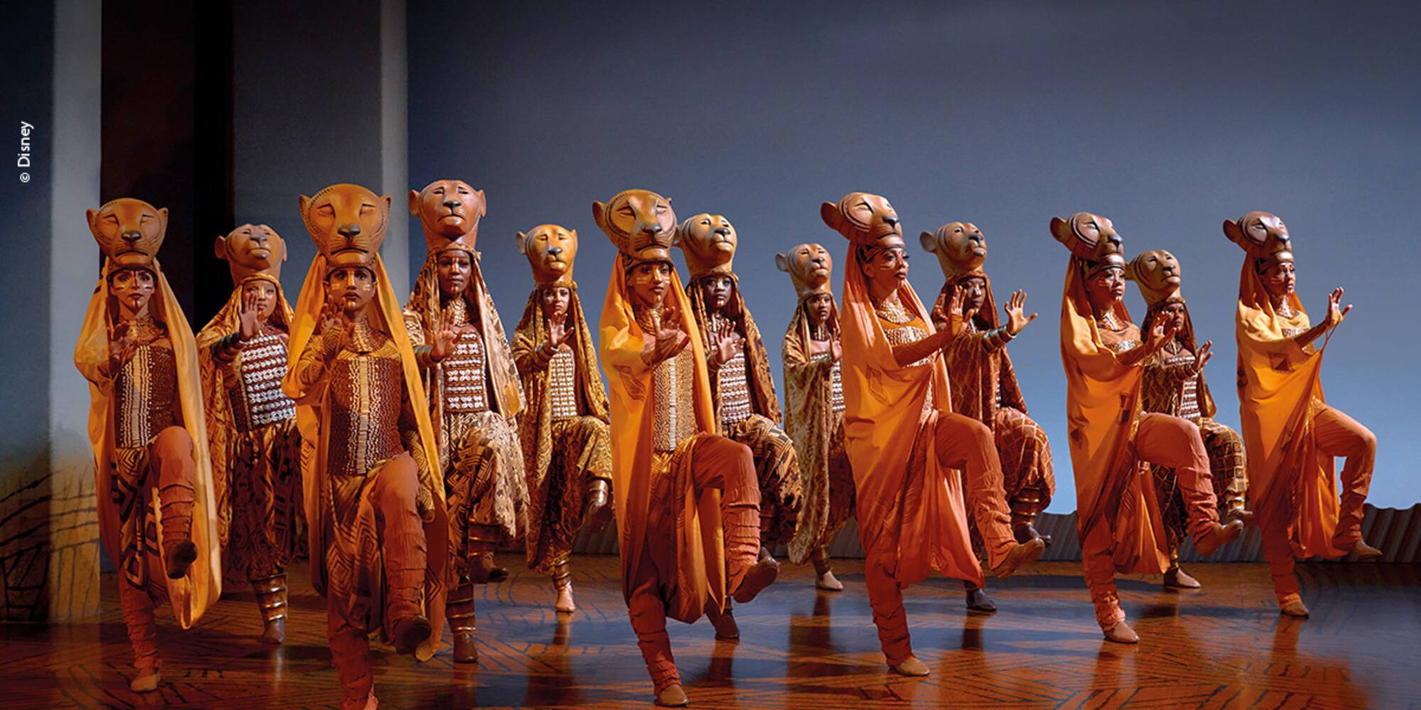 Lion King musical performers in ornate lion mask costumes on stage.