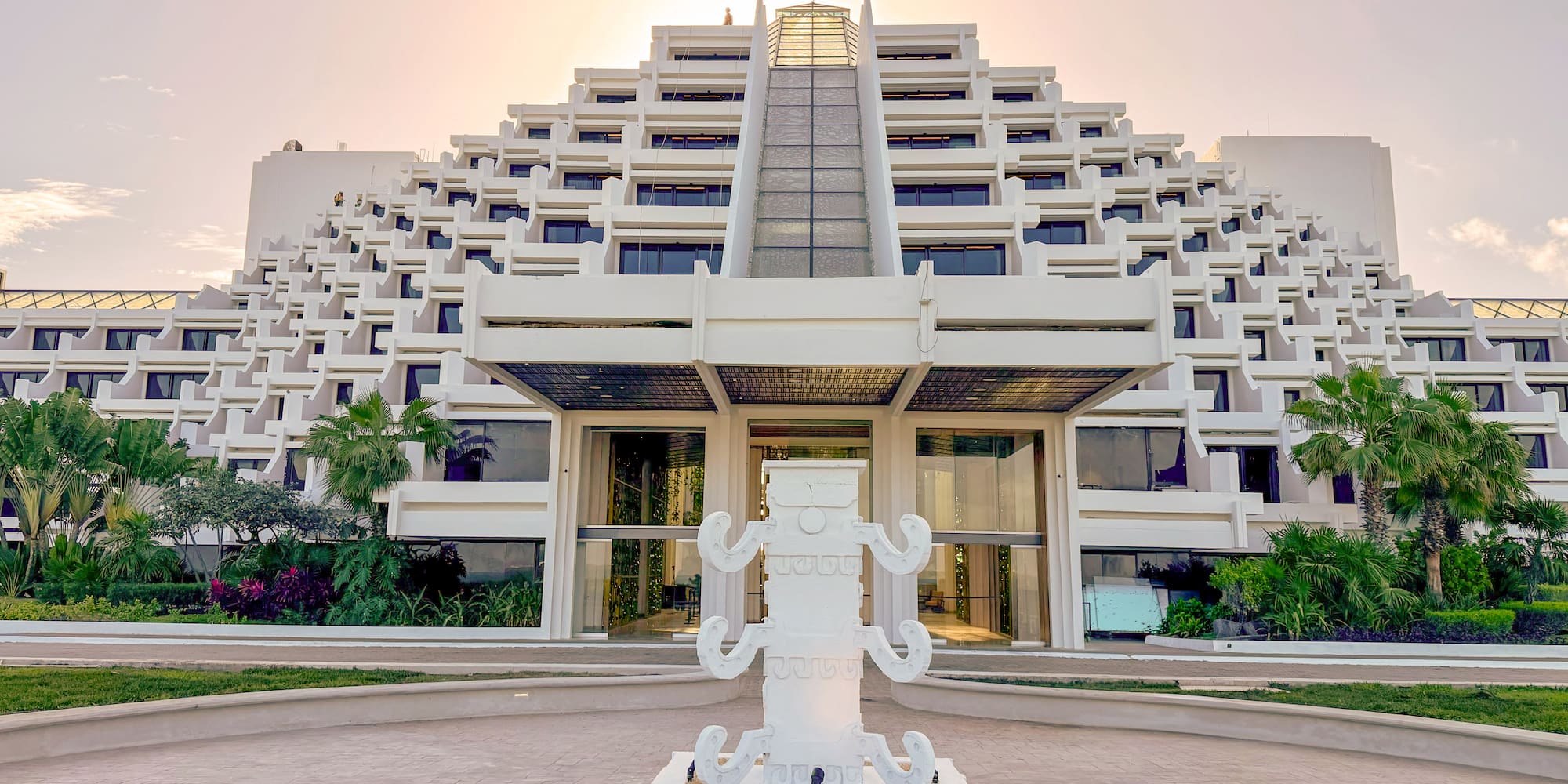 Pyramid-style resort hotel entrance, white sculpture, golden sky.