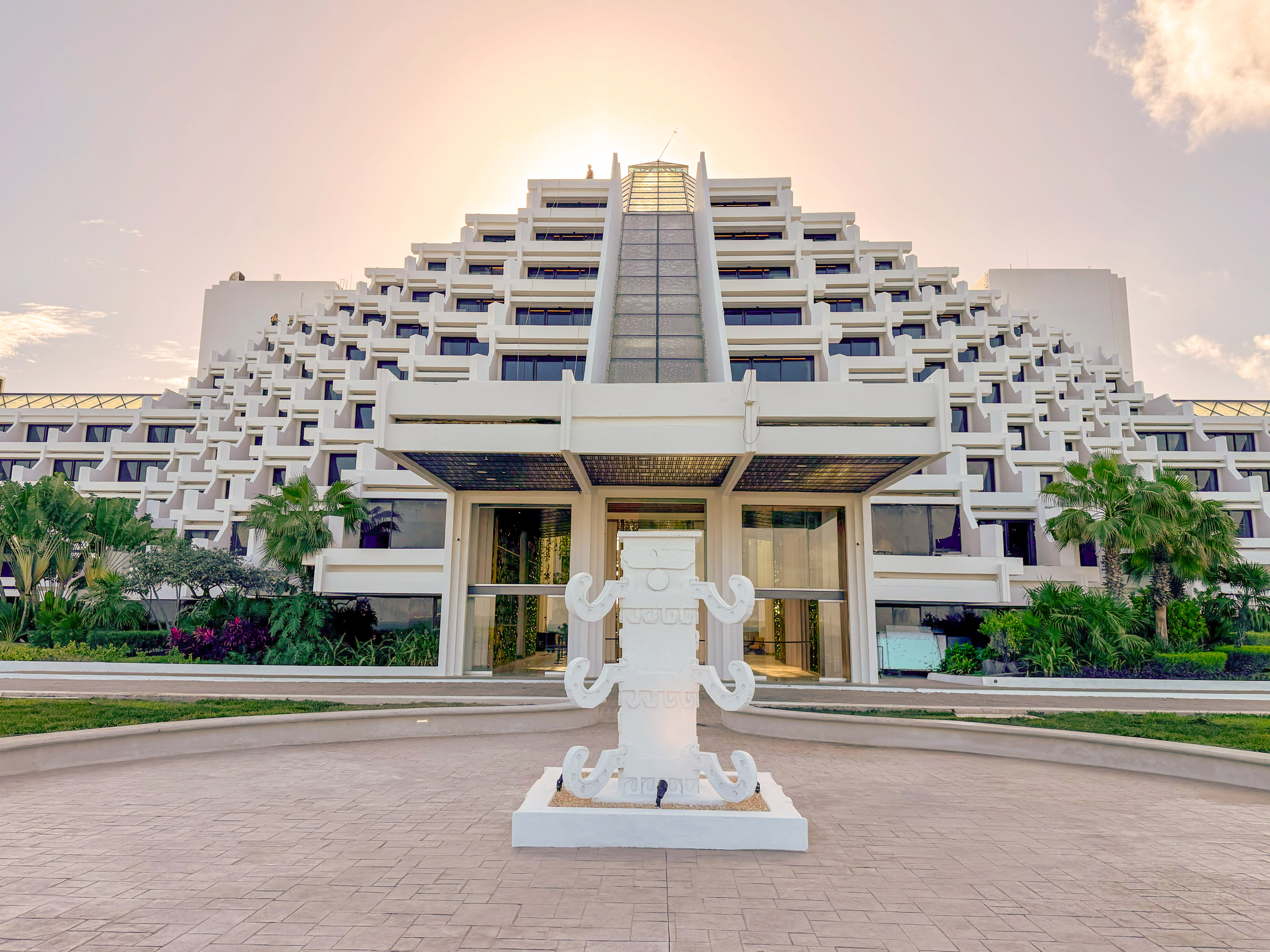 Pyramid-style resort hotel entrance, white sculpture, golden sky.