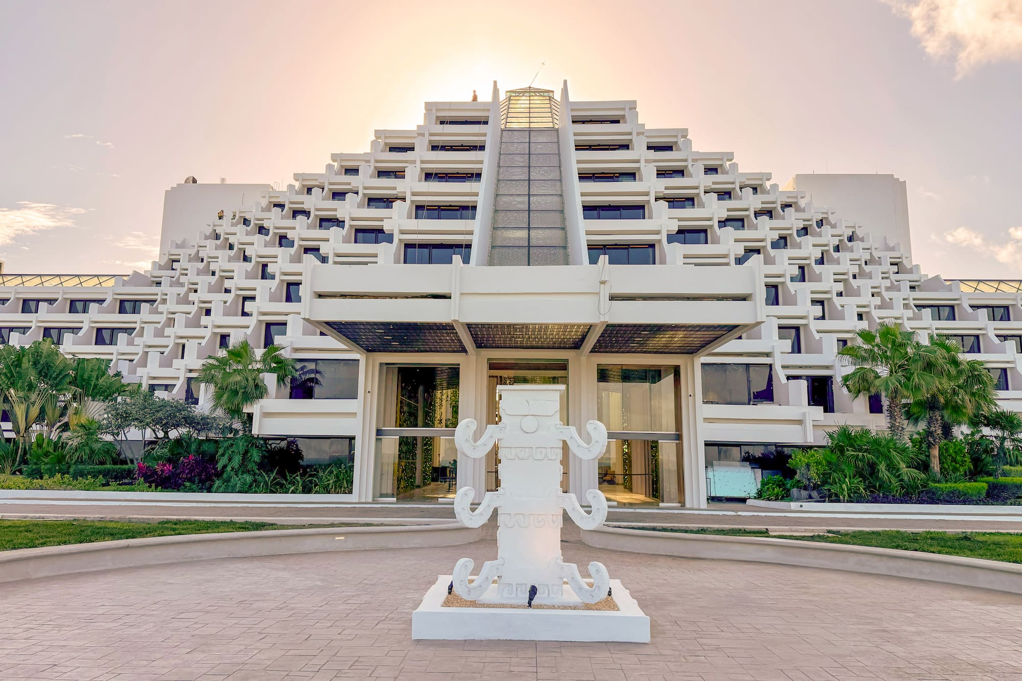Pyramid-style resort hotel entrance, white sculpture, golden sky.