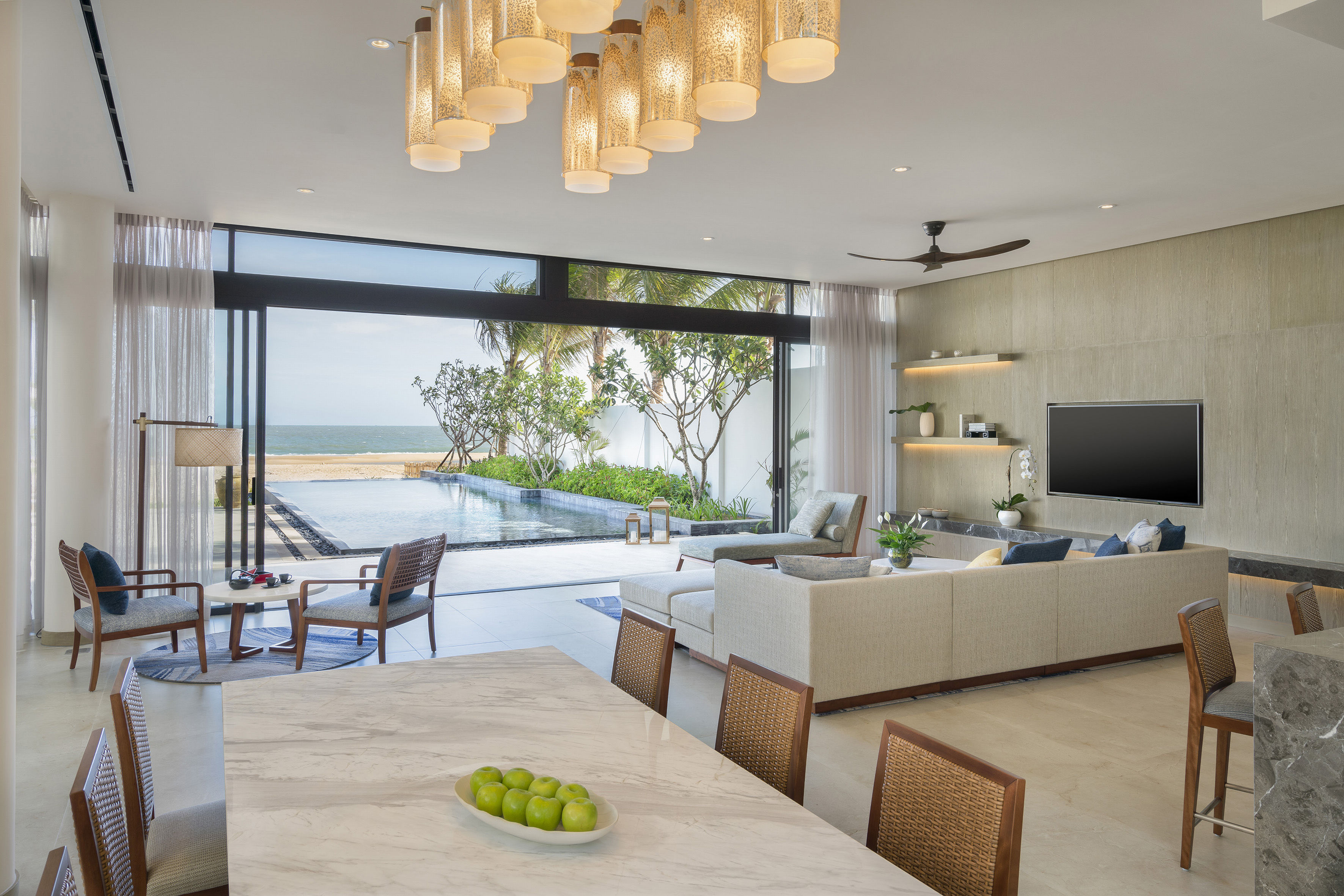 Luxury living room overlooking ocean, beach, and infinity pool; modern design.