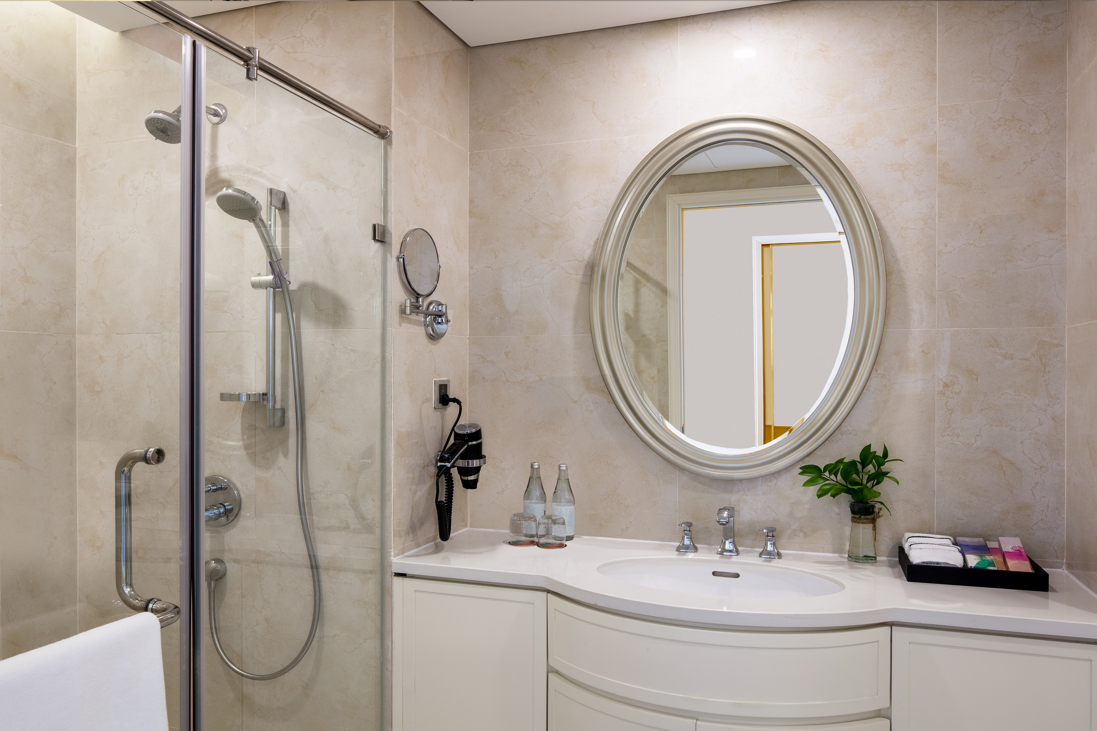 Modern hotel bathroom with glass shower, vanity, and oval mirror.
