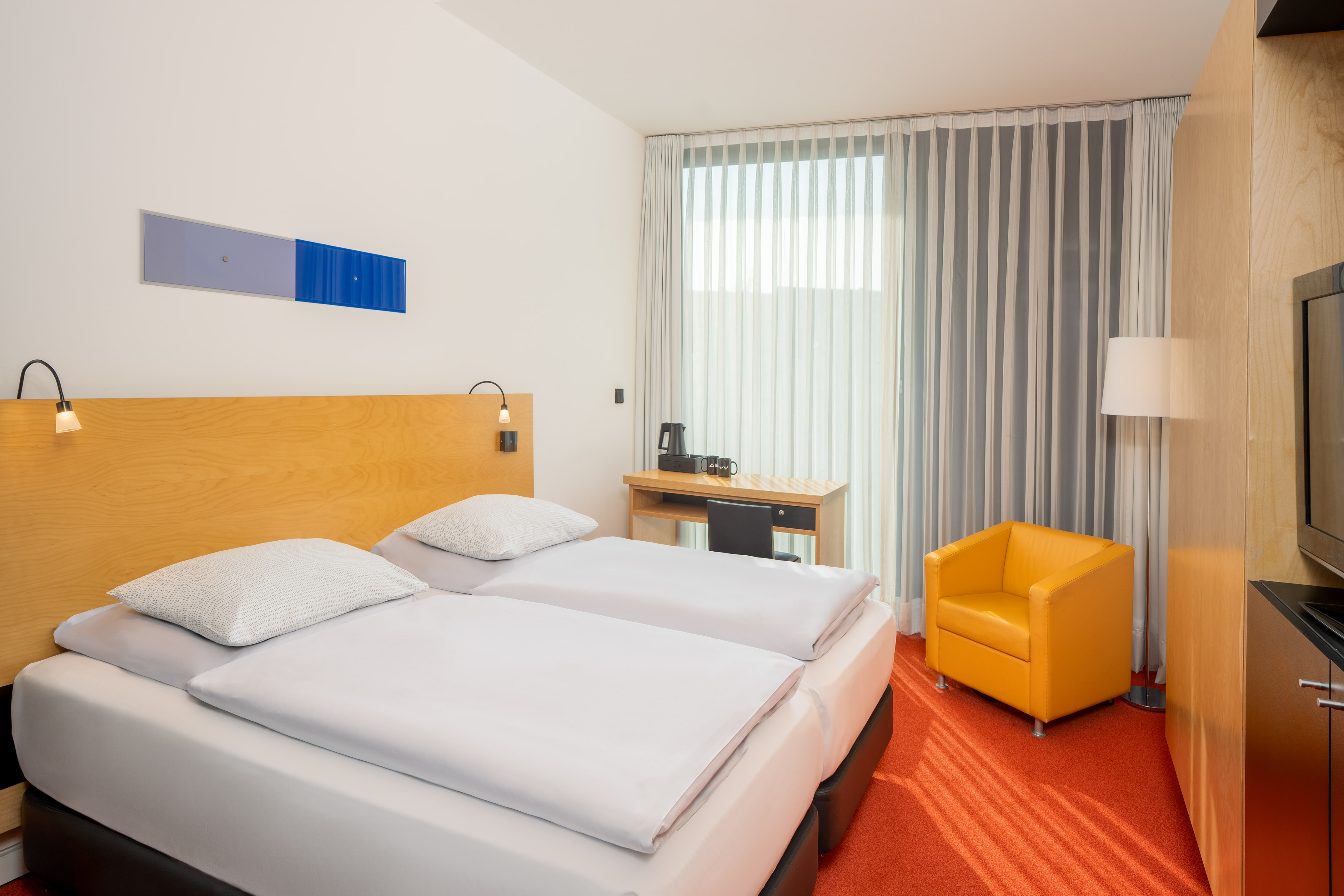 Modern hotel room with twin beds, desk, orange carpet, and yellow armchair. - The INNSiDE Room - INNSiDE Düsseldorf Seestern, Düsseldorf