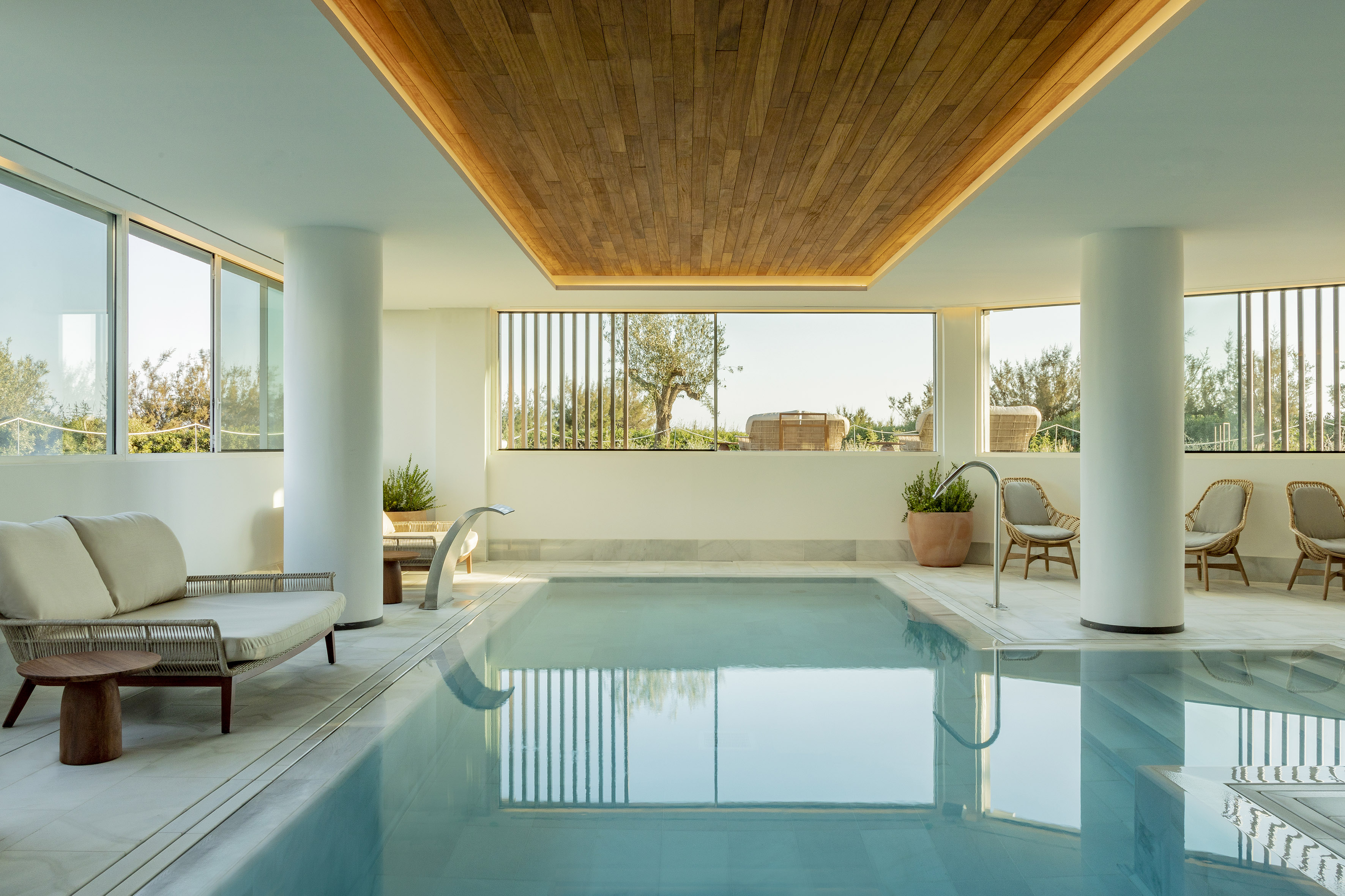 Modern indoor pool in luxury spa with large windows and wooden ceiling.