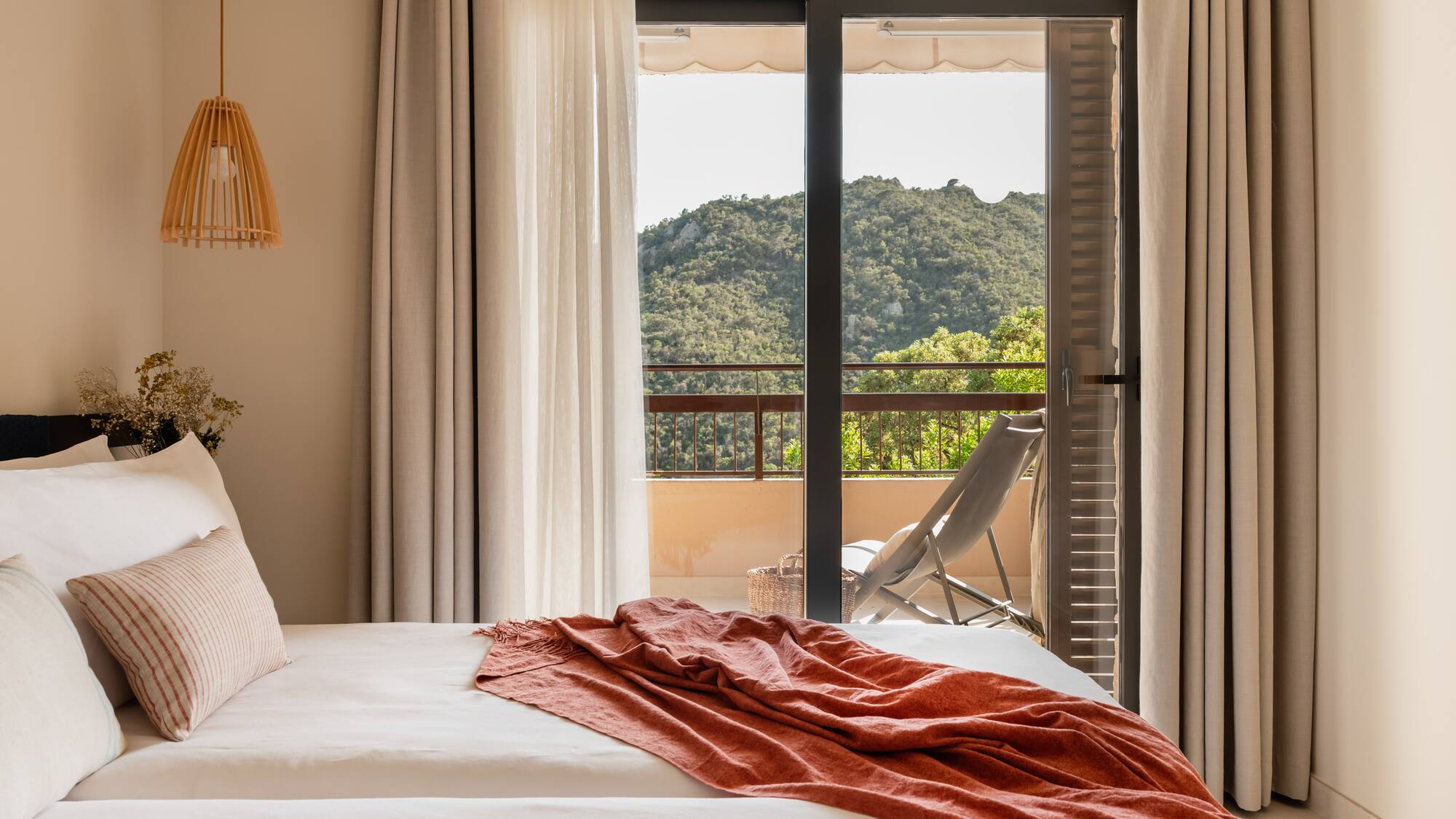 a bed with a red blanket and a chair outside