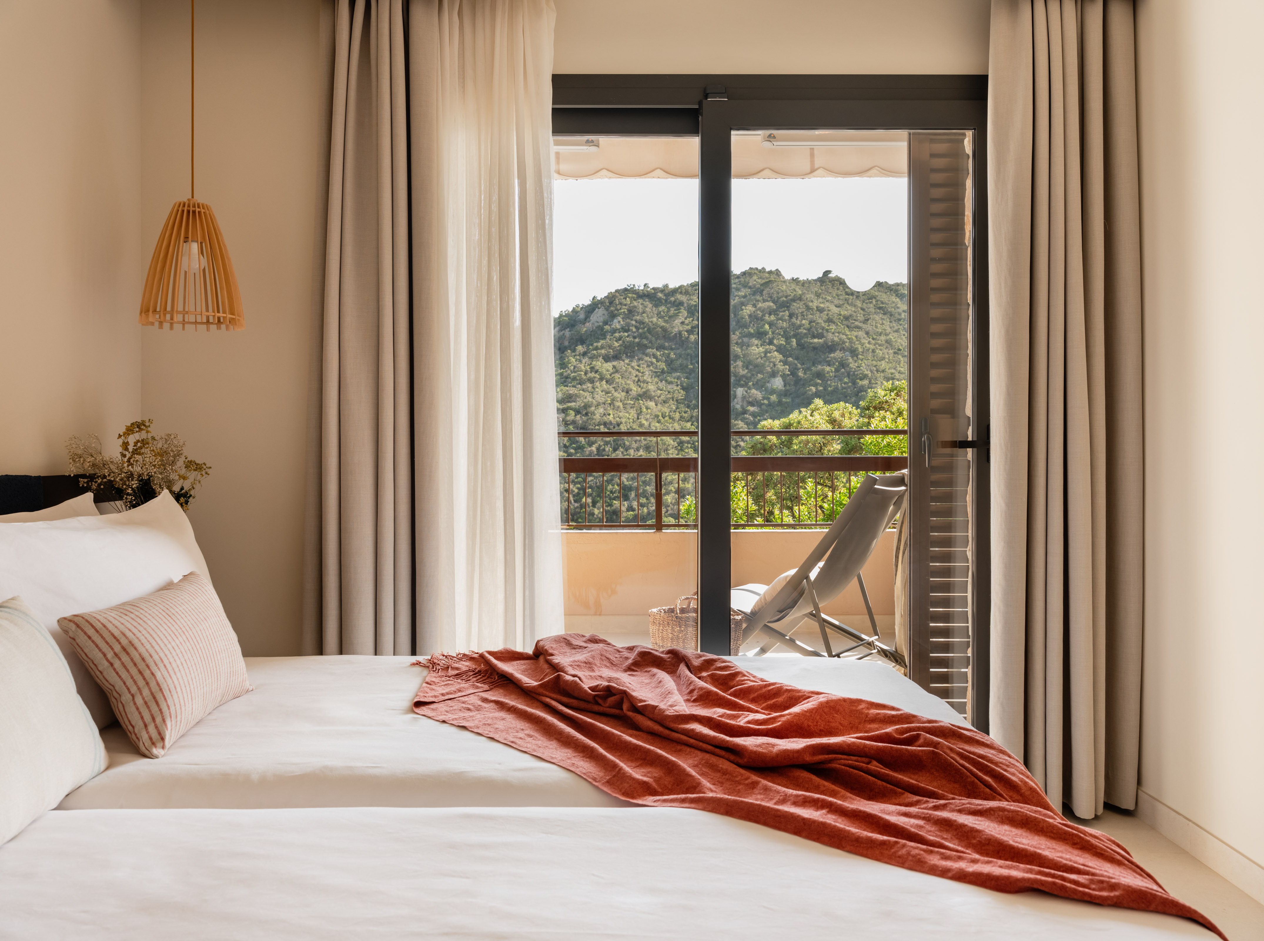 Cozy hotel bedroom with balcony, mountain view, white bed, and orange blanket.