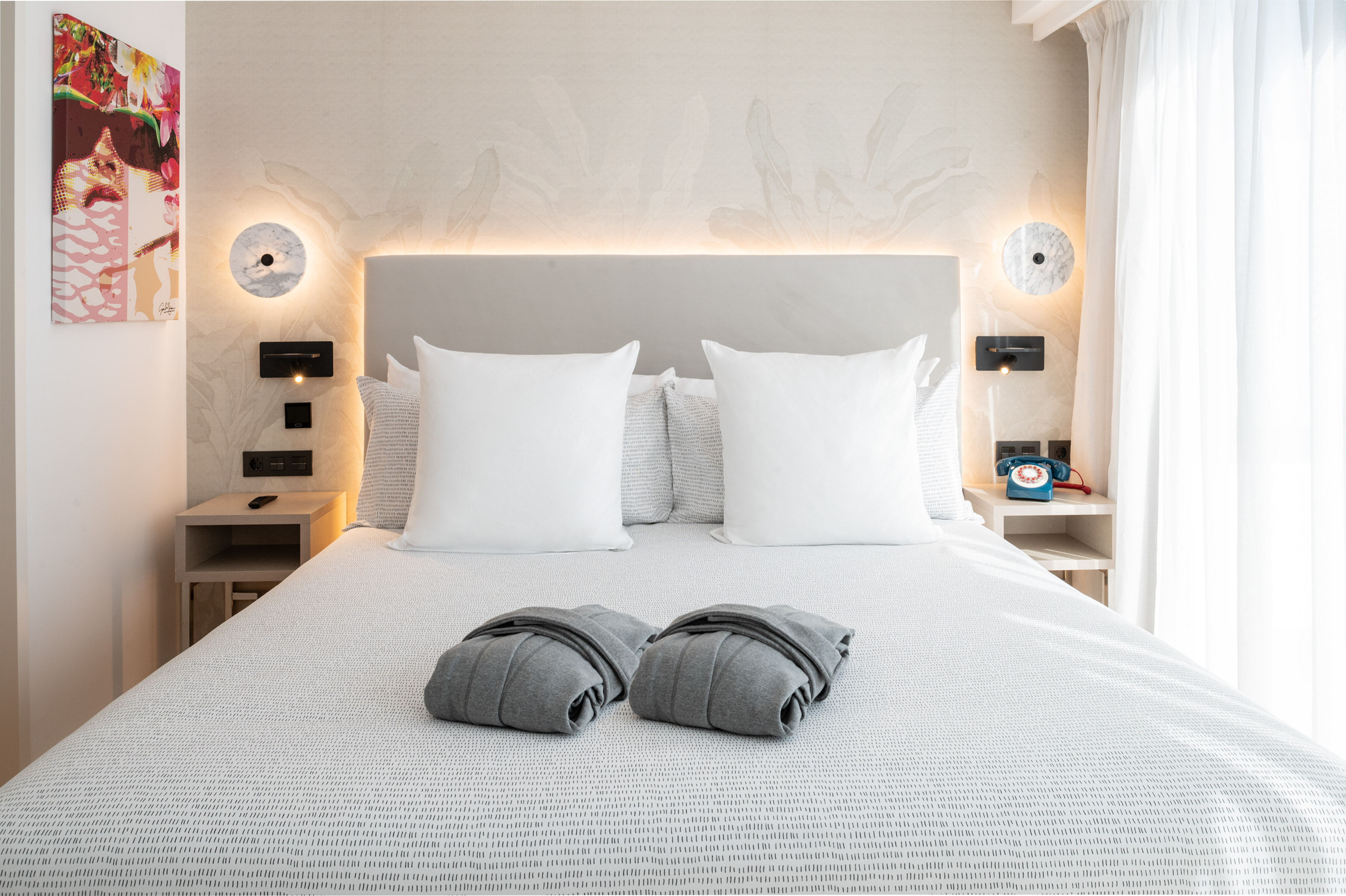 Modern hotel bedroom with comfortable bed, grey robes, and stylish decor.