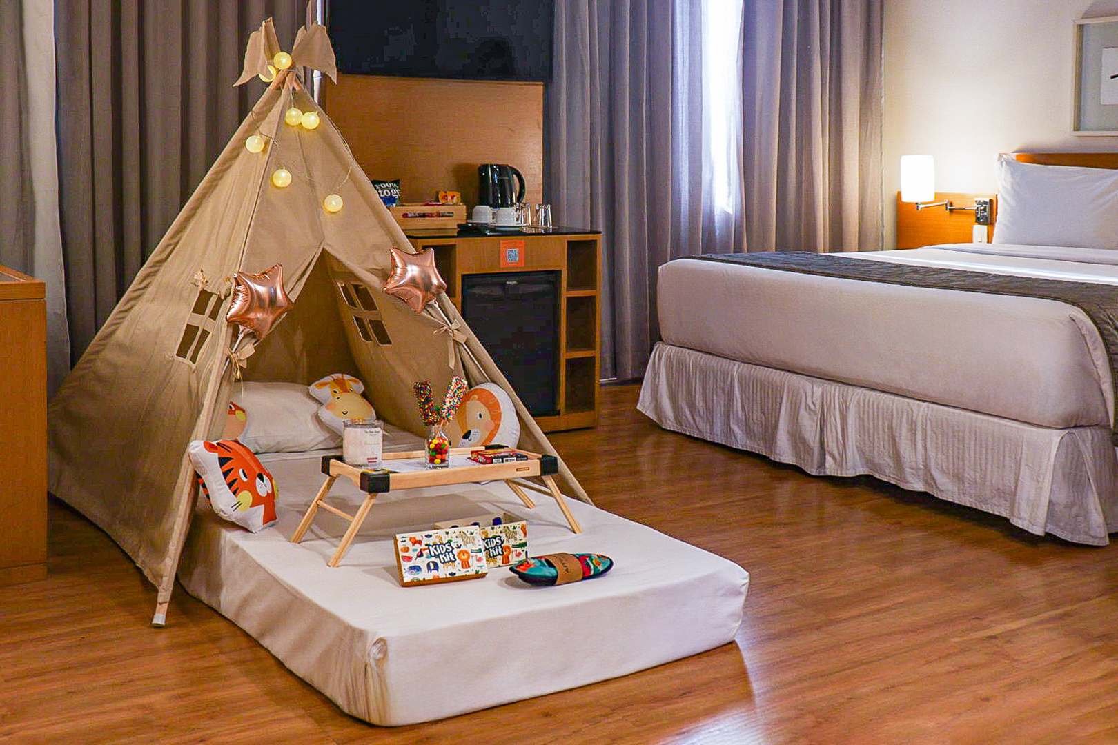 Kids' themed hotel room with a teepee tent, animal pillows, and treats.