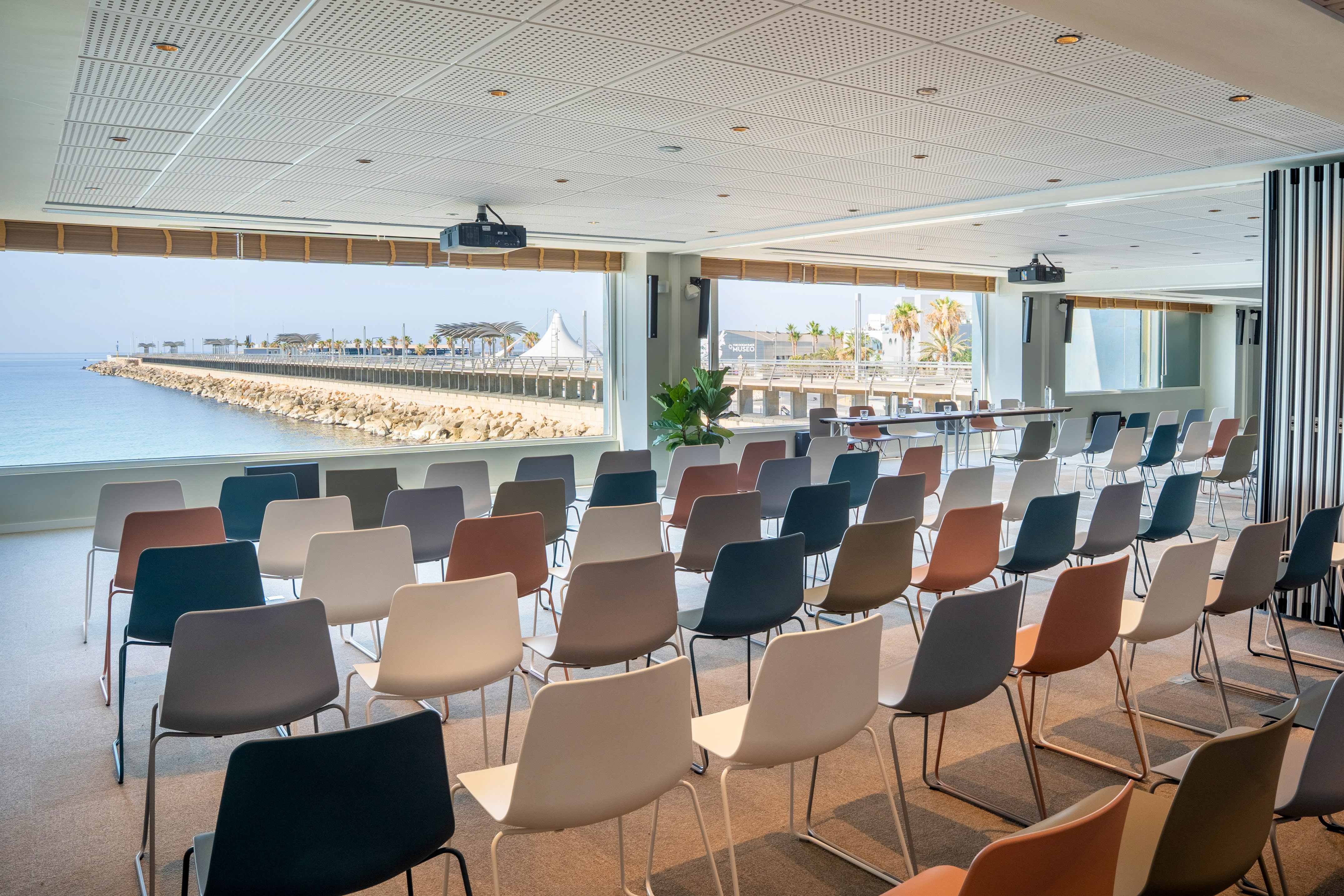 Modern conference room with multi-colored chairs, projector, and sea view.