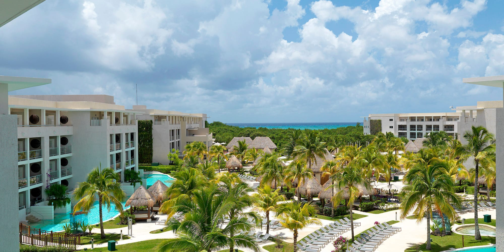 Tropical luxury resort with lagoon pools, palm trees, hotel buildings, ocean.