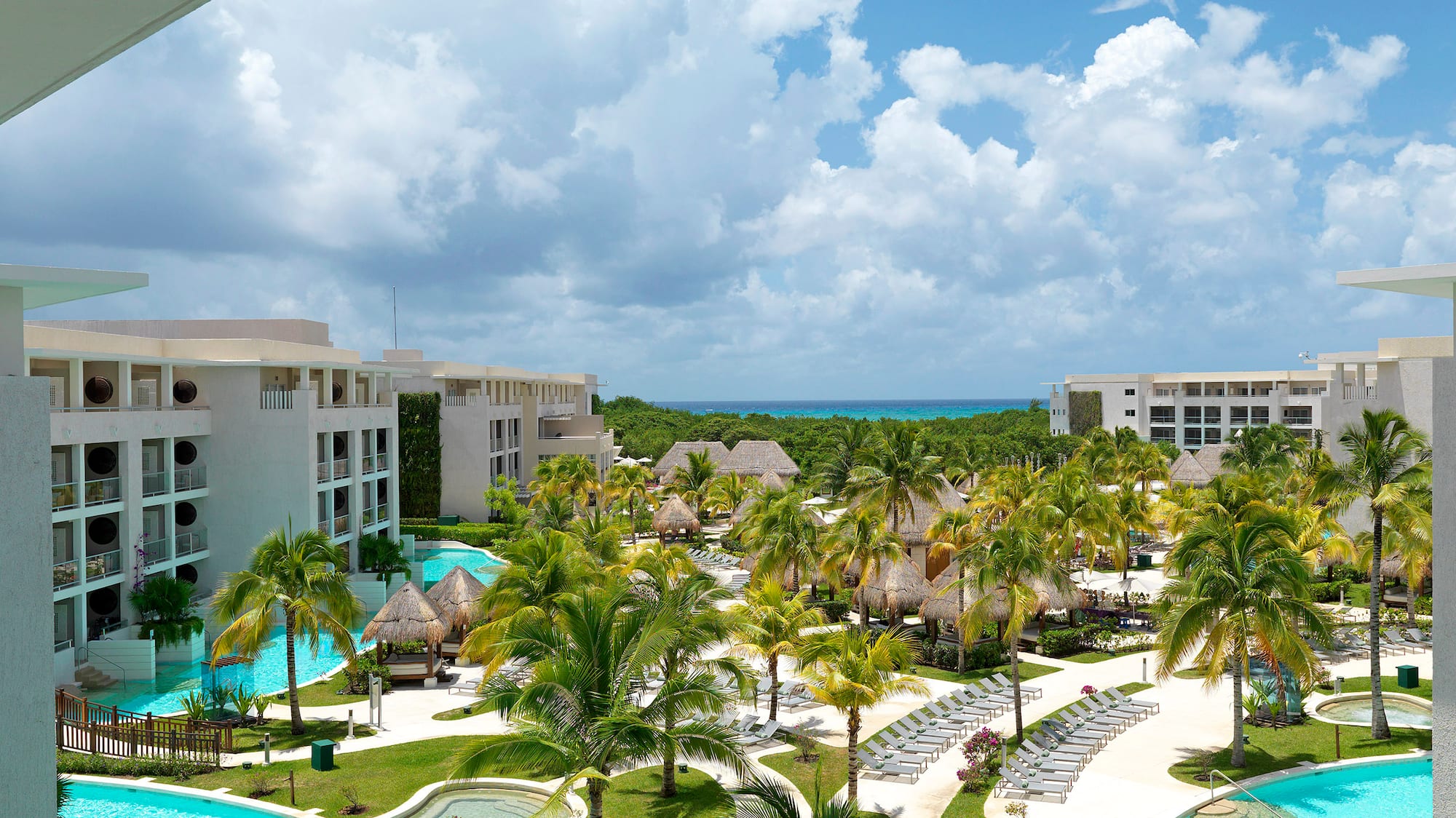 Tropical luxury resort with lagoon pools, palm trees, hotel buildings, ocean.