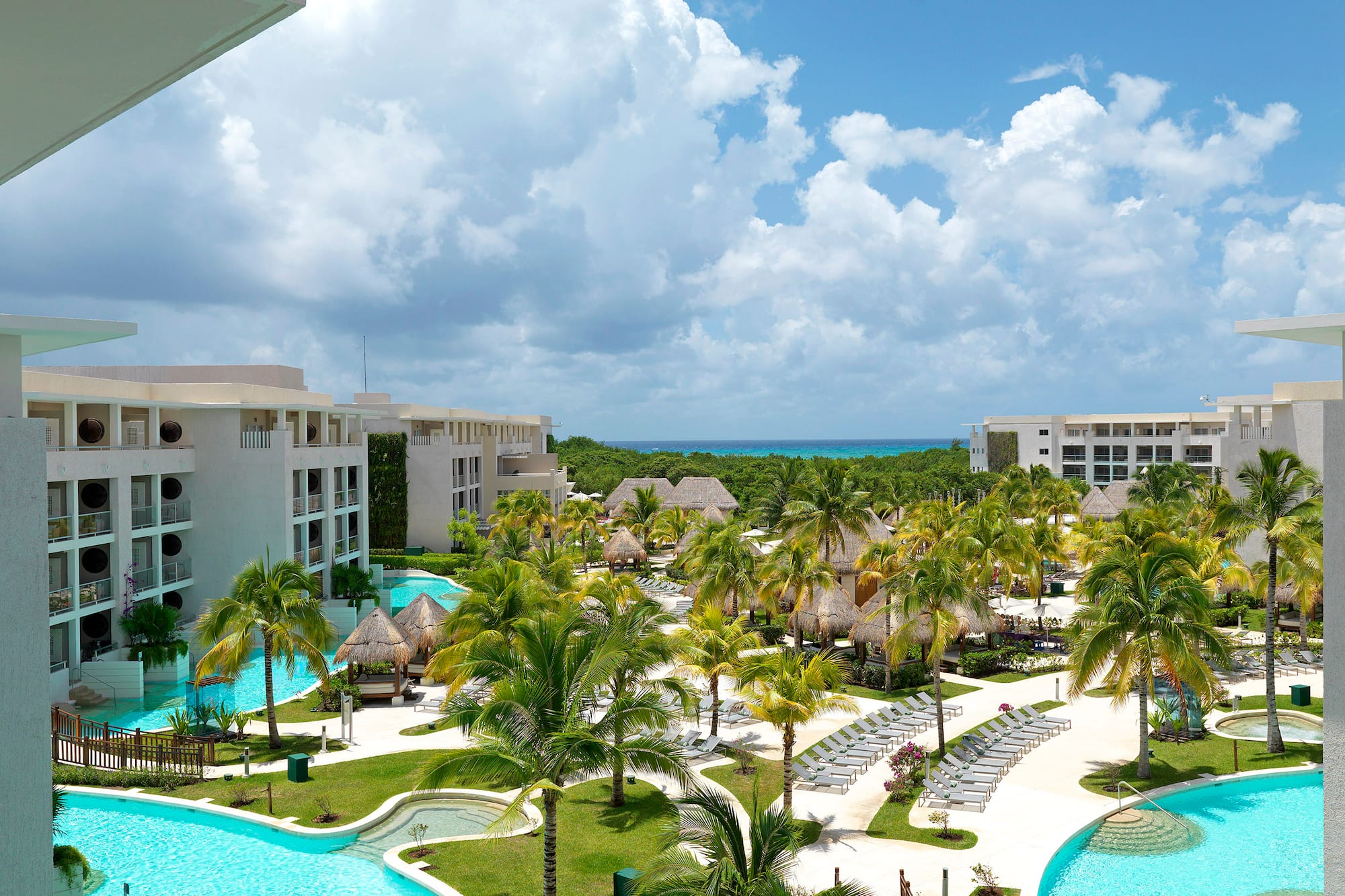 Tropical luxury resort with lagoon pools, palm trees, hotel buildings, ocean.