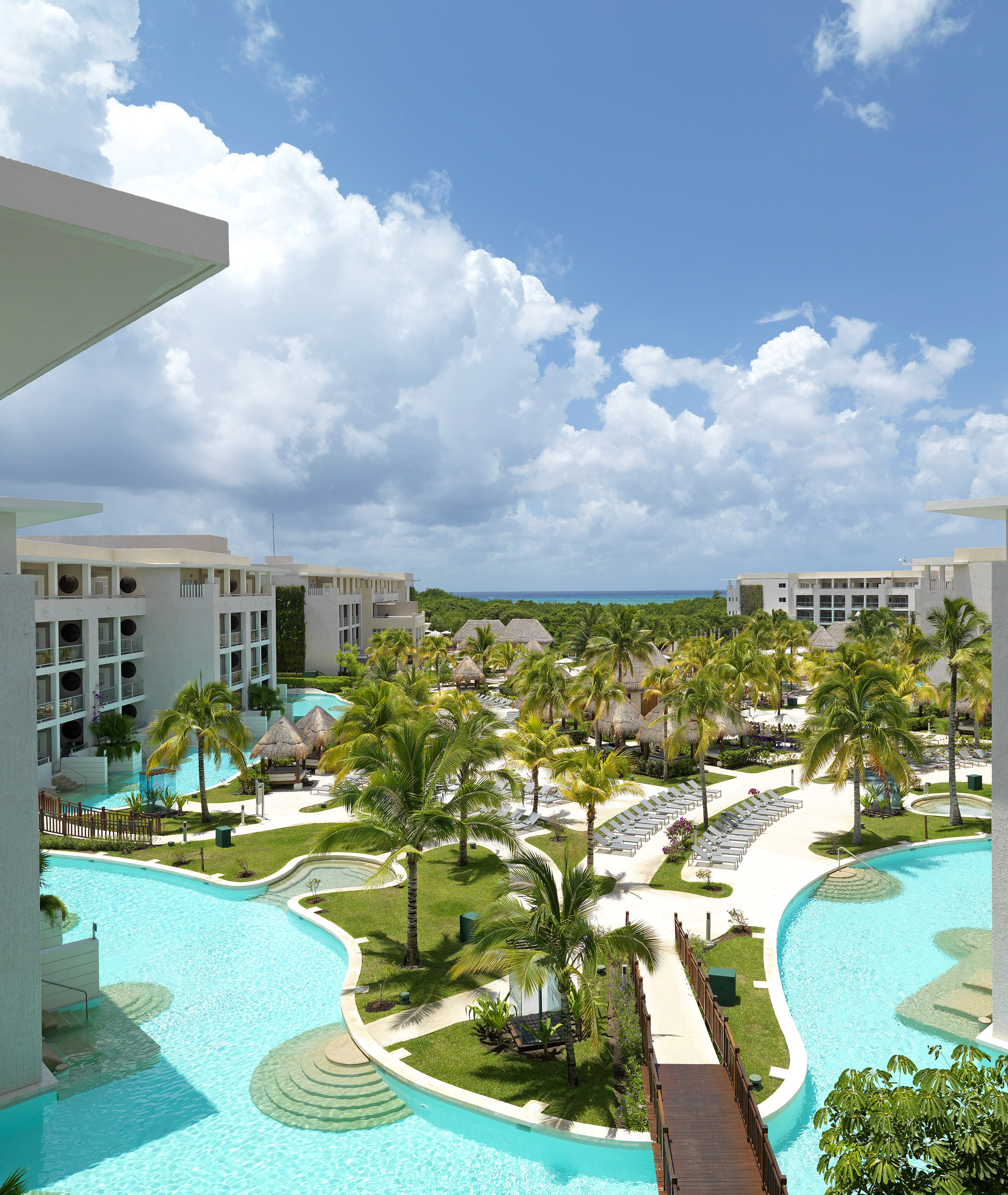 Tropical luxury resort with lagoon pools, palm trees, hotel buildings, ocean.