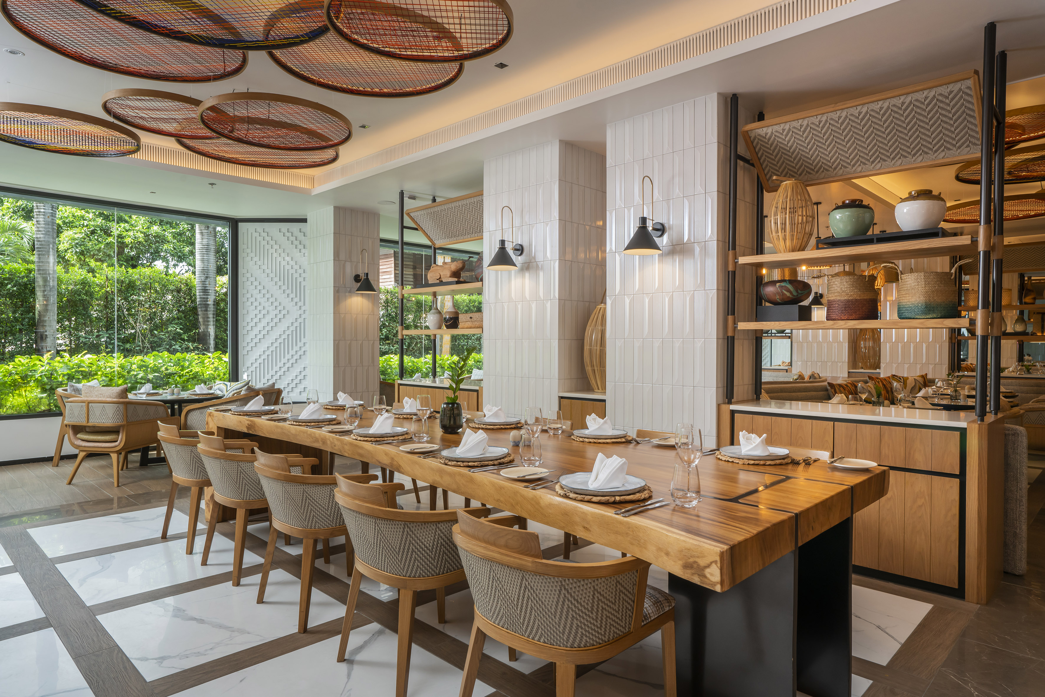 Modern dining room with long wooden table, natural decor, tropical view.