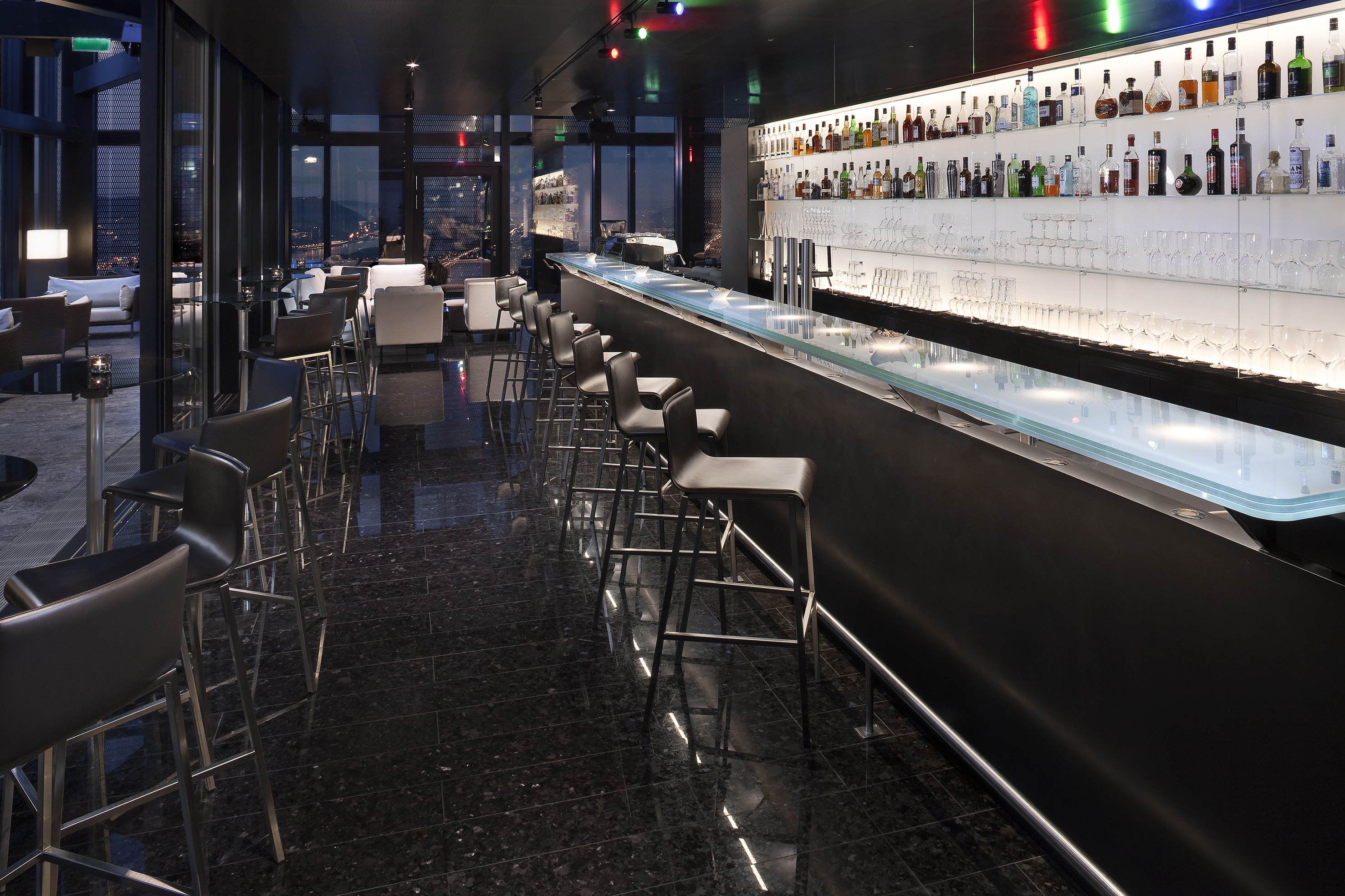 Chic rooftop bar with glowing counter, stocked spirits, and stunning city night view.