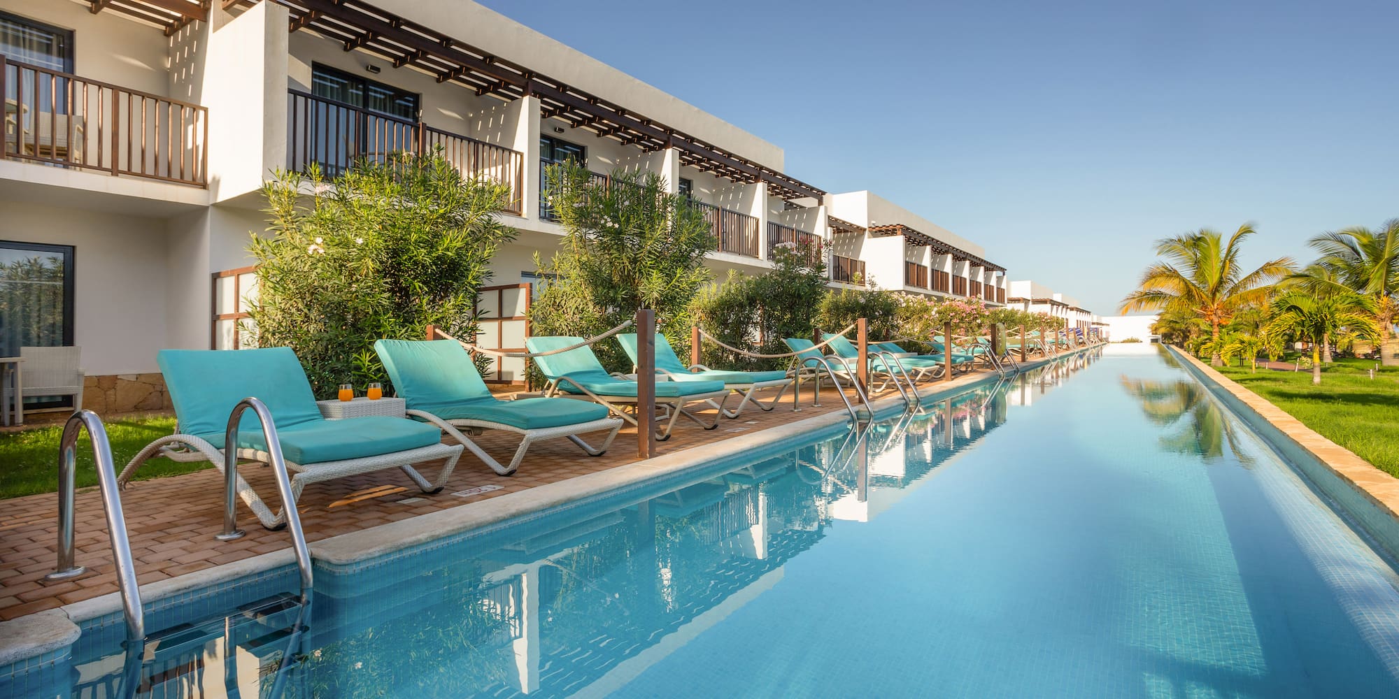a pool with lounge chairs and trees in front of a building