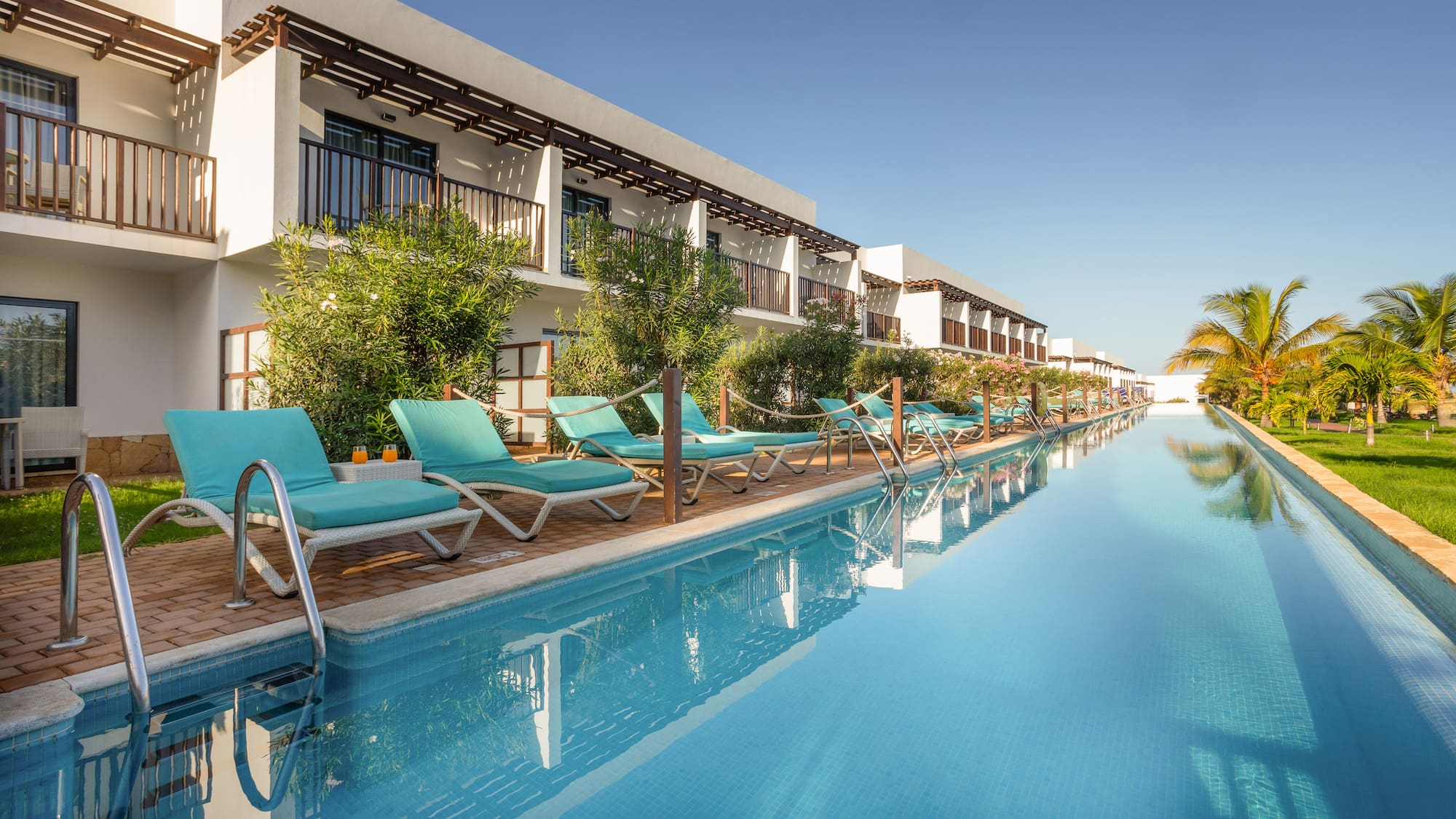 a pool with lounge chairs and trees in front of a building