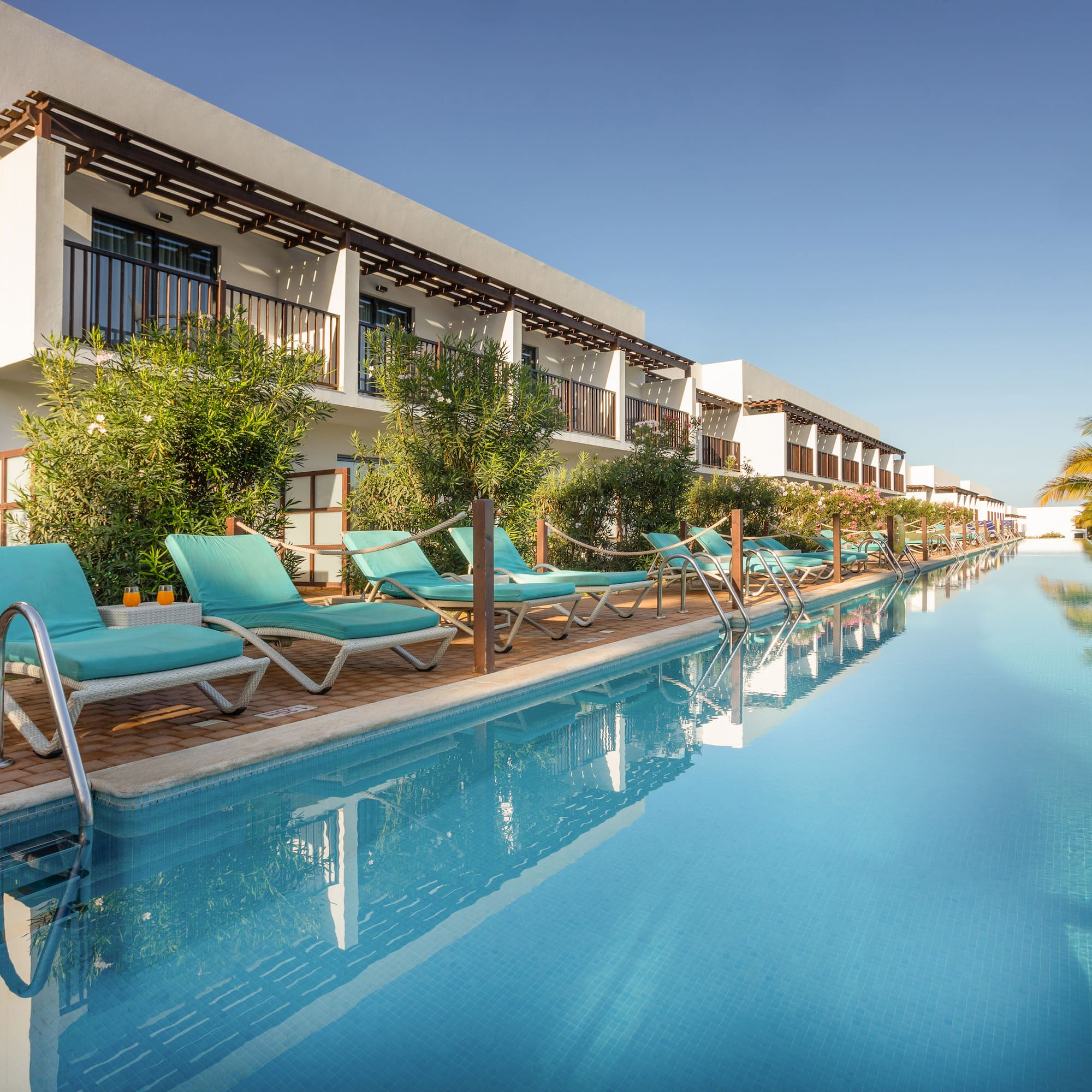 a pool with lounge chairs and trees in front of a building