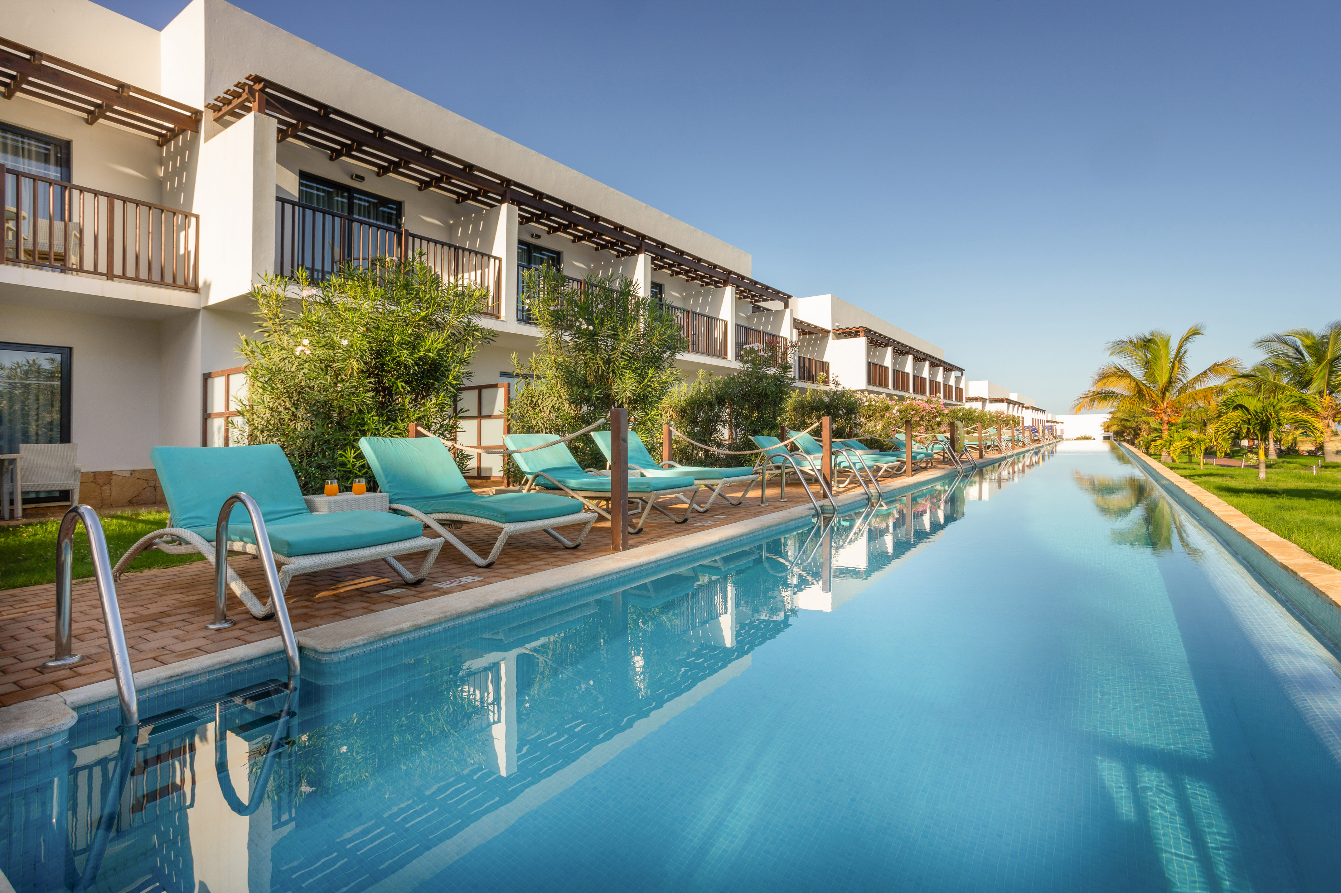 a pool with lounge chairs and trees in front of a building
