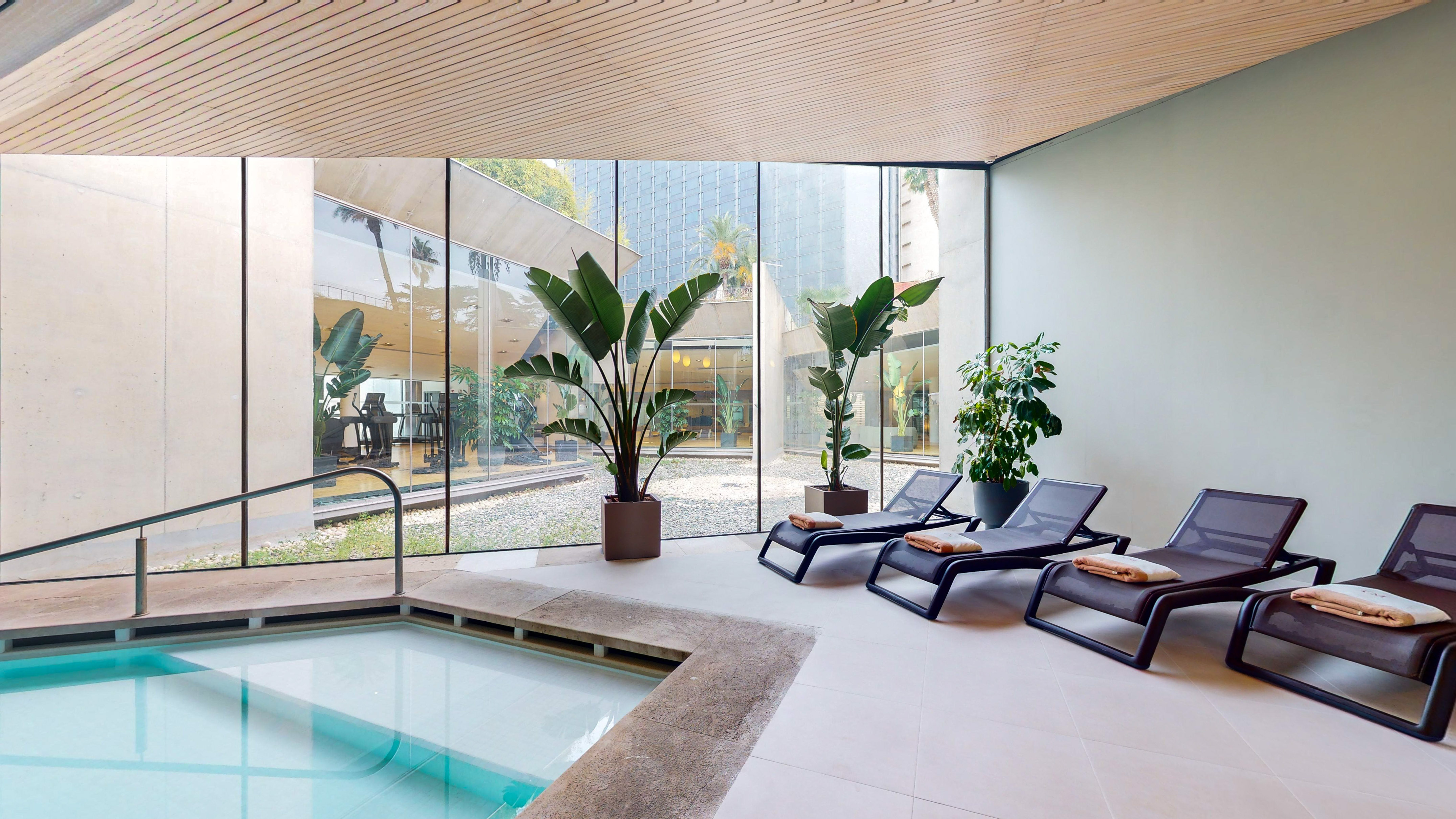 a pool with lounge chairs and plants in a room with windows