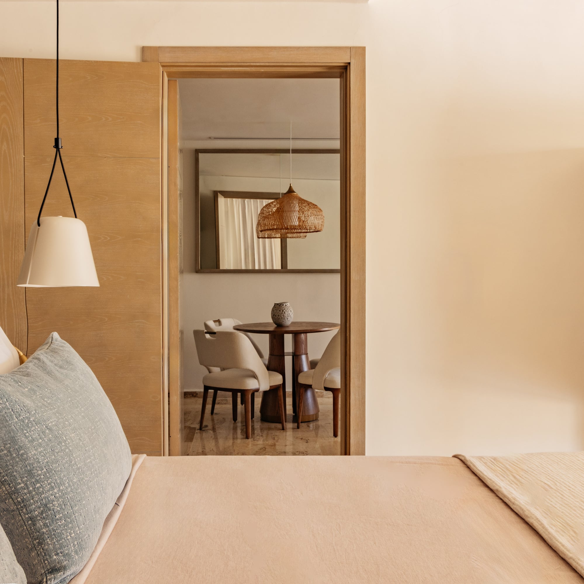 Modern hotel bedroom, view to living area with wood table, wicker light.